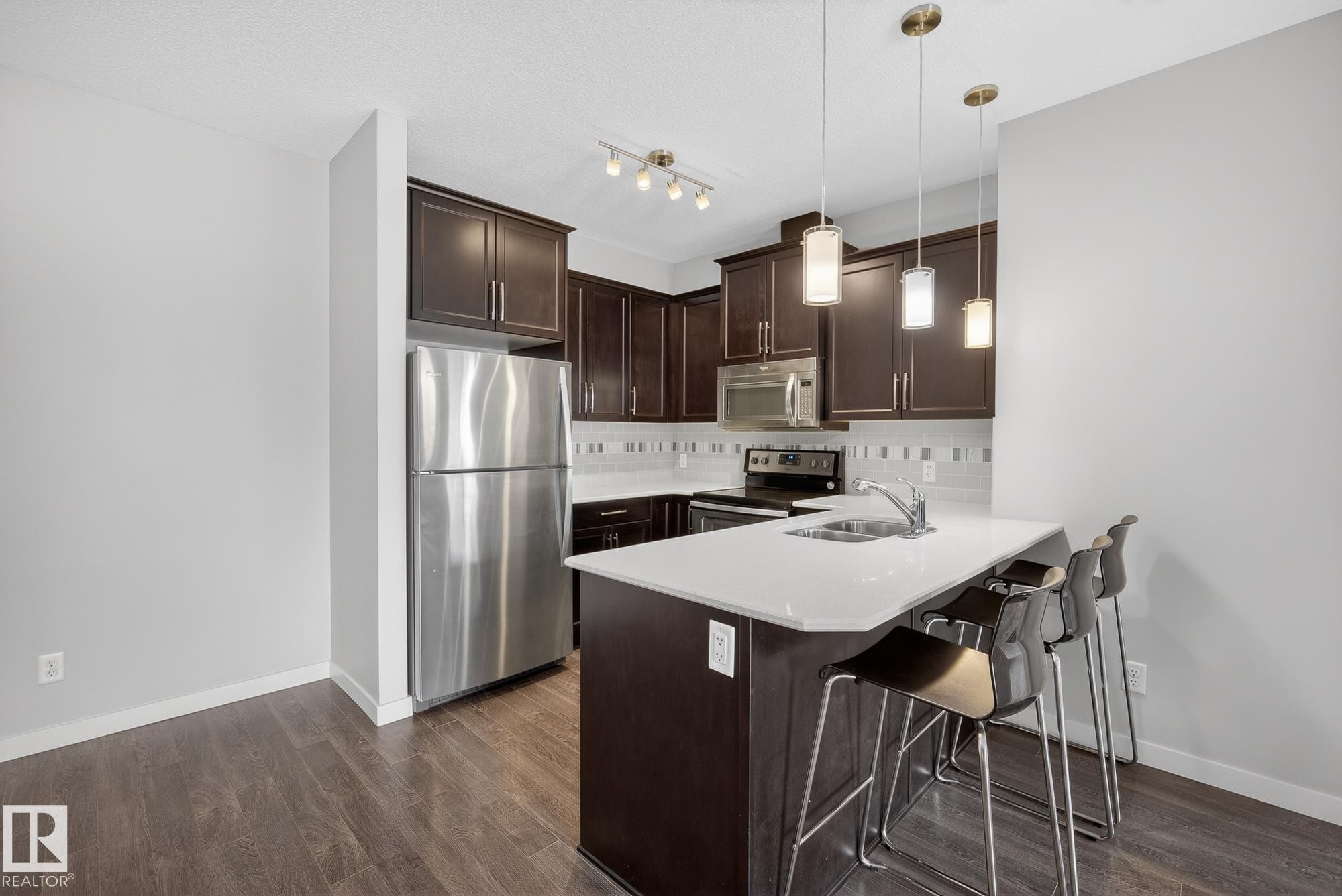 Kitchen with dark wood finish cabinetry, stainless steel appliances, a kitchen bar, decorative backsplash, and a peninsula - 206 812 Welsh Drive, Edmonton, AB - Indoor Photo Showing Kitchen With Stainless Steel Kitchen With Double Sink
