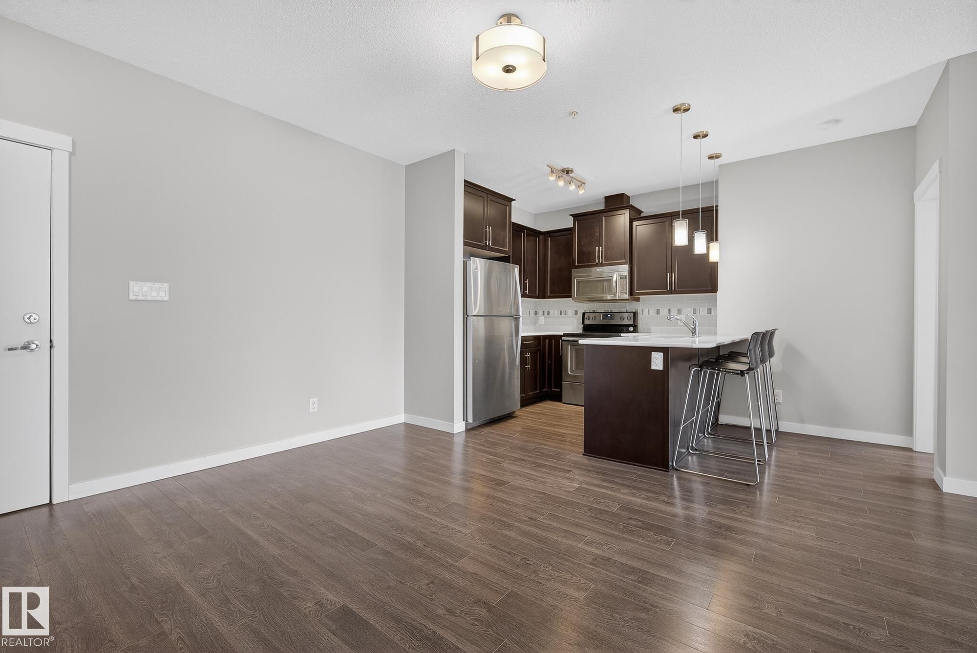 Kitchen with stainless steel appliances, a peninsula, dark wood finish cabinetry, dark wood finished floors, and hanging light fixtures - 206 812 Welsh Drive, Edmonton, AB - Indoor Photo Showing Kitchen