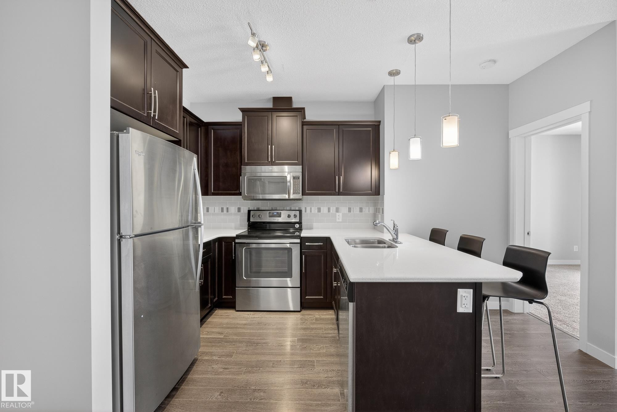 Kitchen featuring a peninsula, a kitchen bar, stainless steel appliances, dark wood finish cabinets, and tasteful backsplash - 206 812 Welsh Drive, Edmonton, AB - Indoor Photo Showing Kitchen With Stainless Steel Kitchen With Double Sink