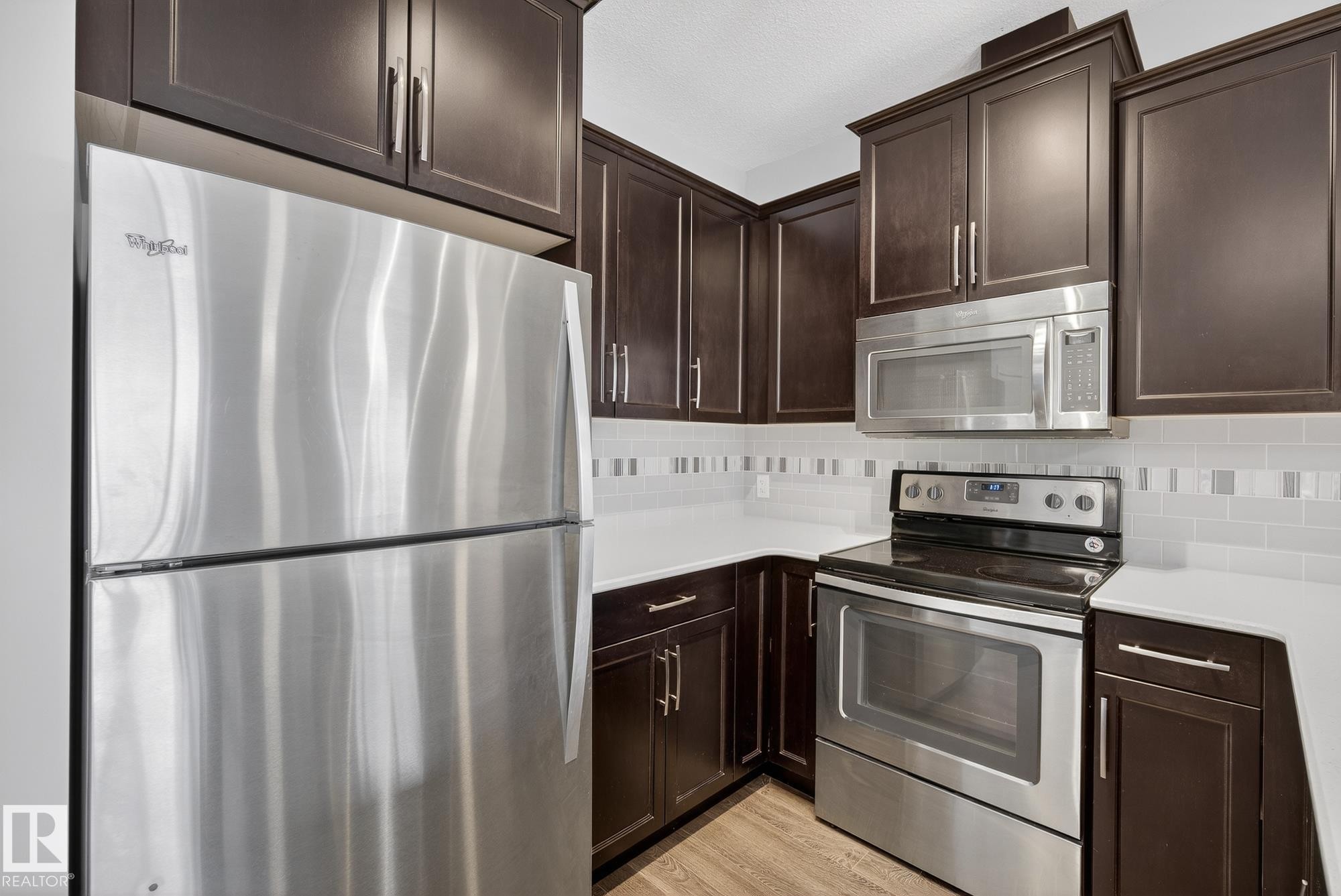 Kitchen with stainless steel appliances, dark wood finish cabinets, light countertops, and decorative backsplash - 206 812 Welsh Drive, Edmonton, AB - Indoor Photo Showing Kitchen With Stainless Steel Kitchen