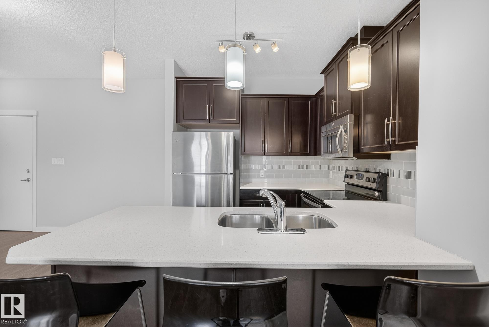Kitchen with a peninsula, stainless steel appliances, a breakfast bar area, dark wood finish cabinets, and backsplash - 206 812 Welsh Drive, Edmonton, AB - Indoor Photo Showing Kitchen With Stainless Steel Kitchen With Double Sink With Upgraded Kitchen