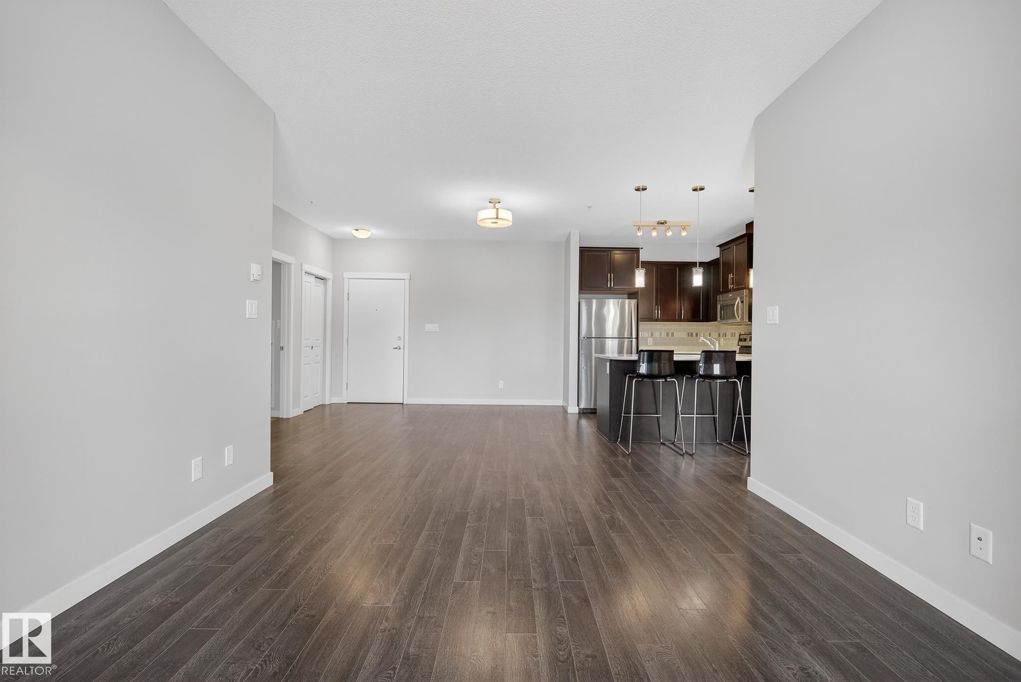 Unfurnished living room with dark wood-style flooring and baseboards - 206 812 Welsh Drive, Edmonton, AB - Indoor