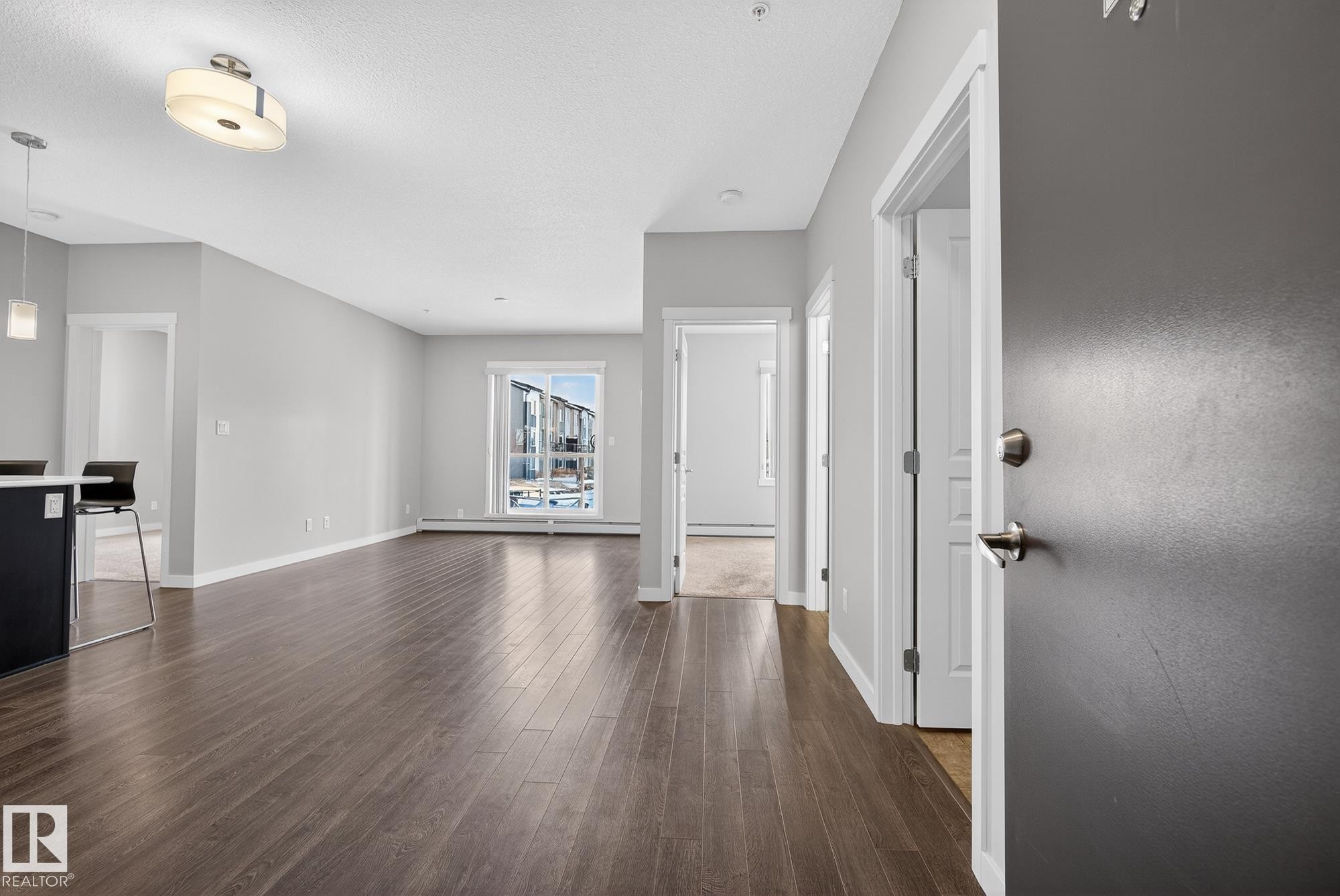 Unfurnished living room featuring dark wood-style flooring, a textured ceiling, and a baseboard radiator - 206 812 Welsh Drive, Edmonton, AB - Indoor Photo Showing Other Room