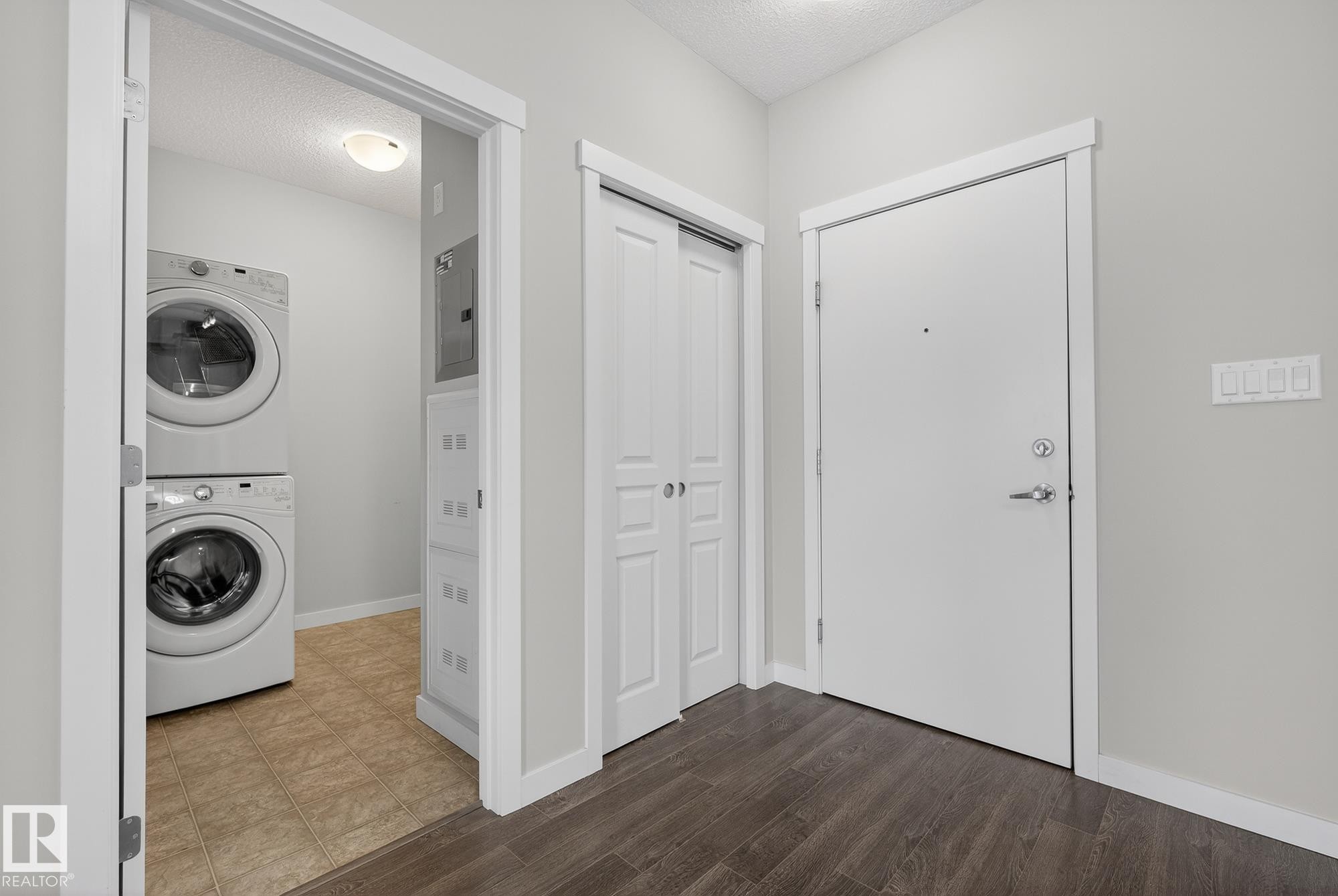 Laundry area with stacked washer and clothes dryer, electric panel, a textured ceiling, and dark wood-type flooring - 206 812 Welsh Drive, Edmonton, AB - Indoor Photo Showing Laundry Room