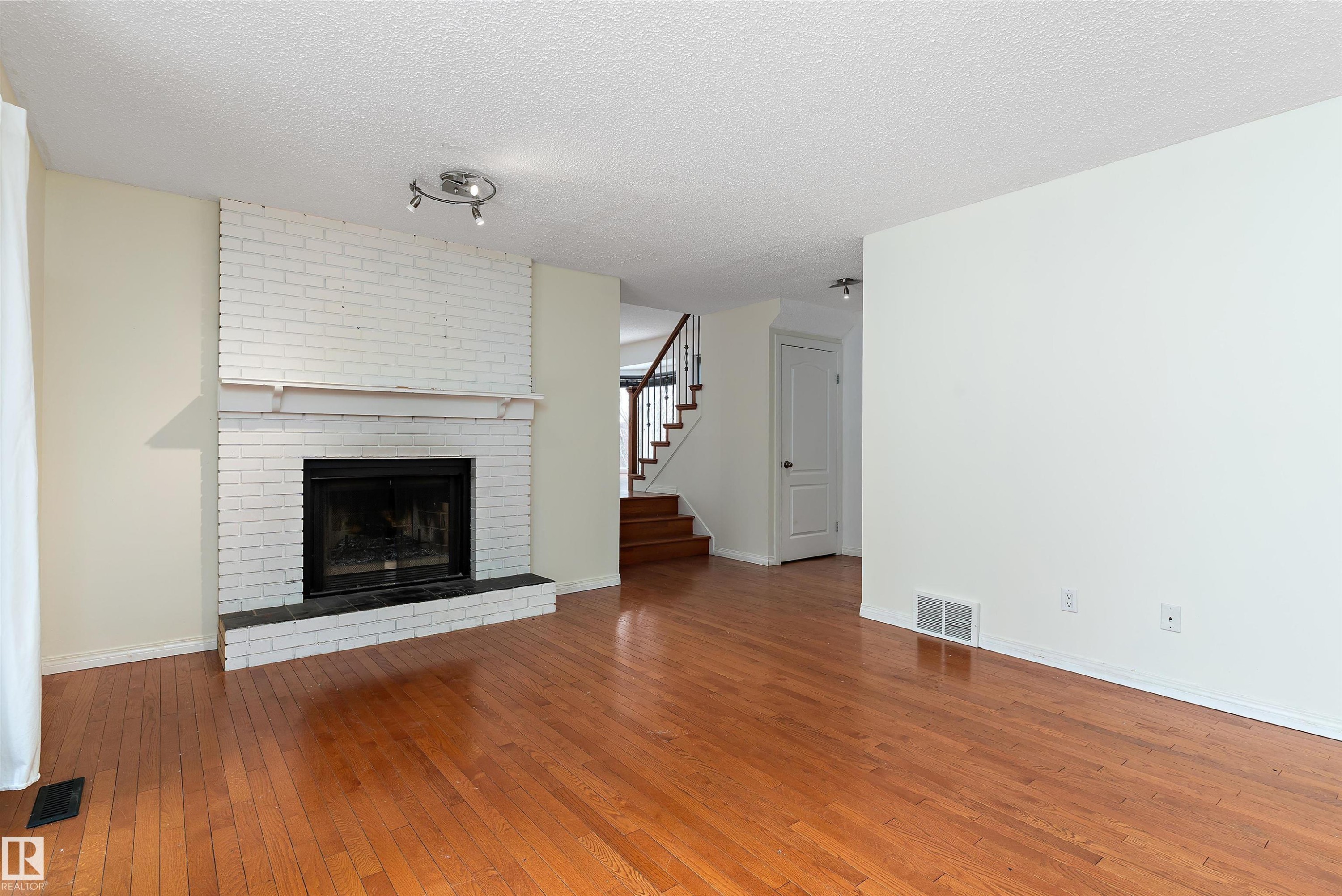 Unfurnished living room with hardwood / wood-style flooring, a textured ceiling, and a brick fireplace - 115 Walker Road, Edmonton, AB - Indoor Photo Showing Living Room With Fireplace