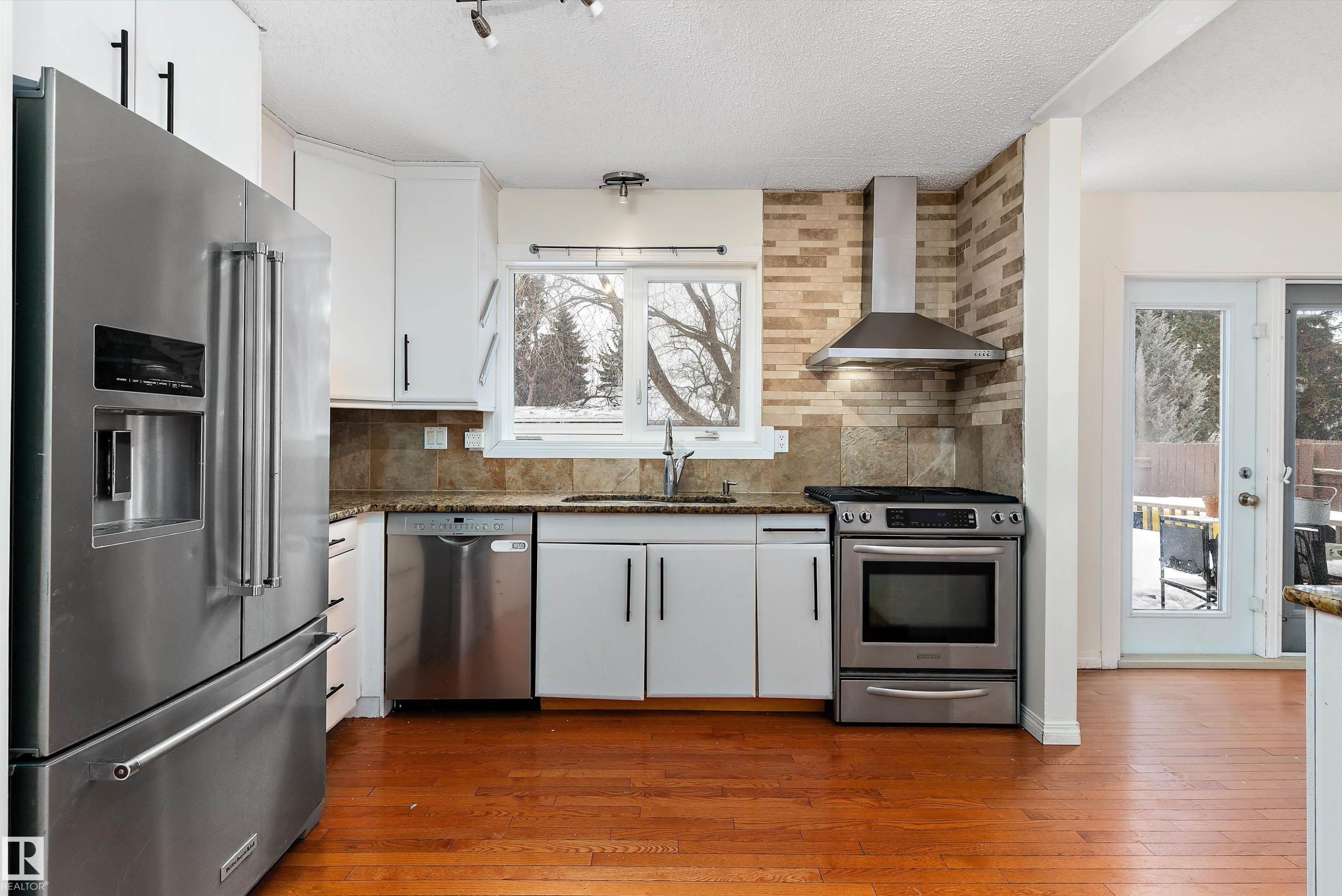 Kitchen with stainless steel appliances, dark stone countertops, white cabinets, tasteful backsplash, and a textured ceiling - 115 Walker Road, Edmonton, AB - Indoor Photo Showing Kitchen With Upgraded Kitchen