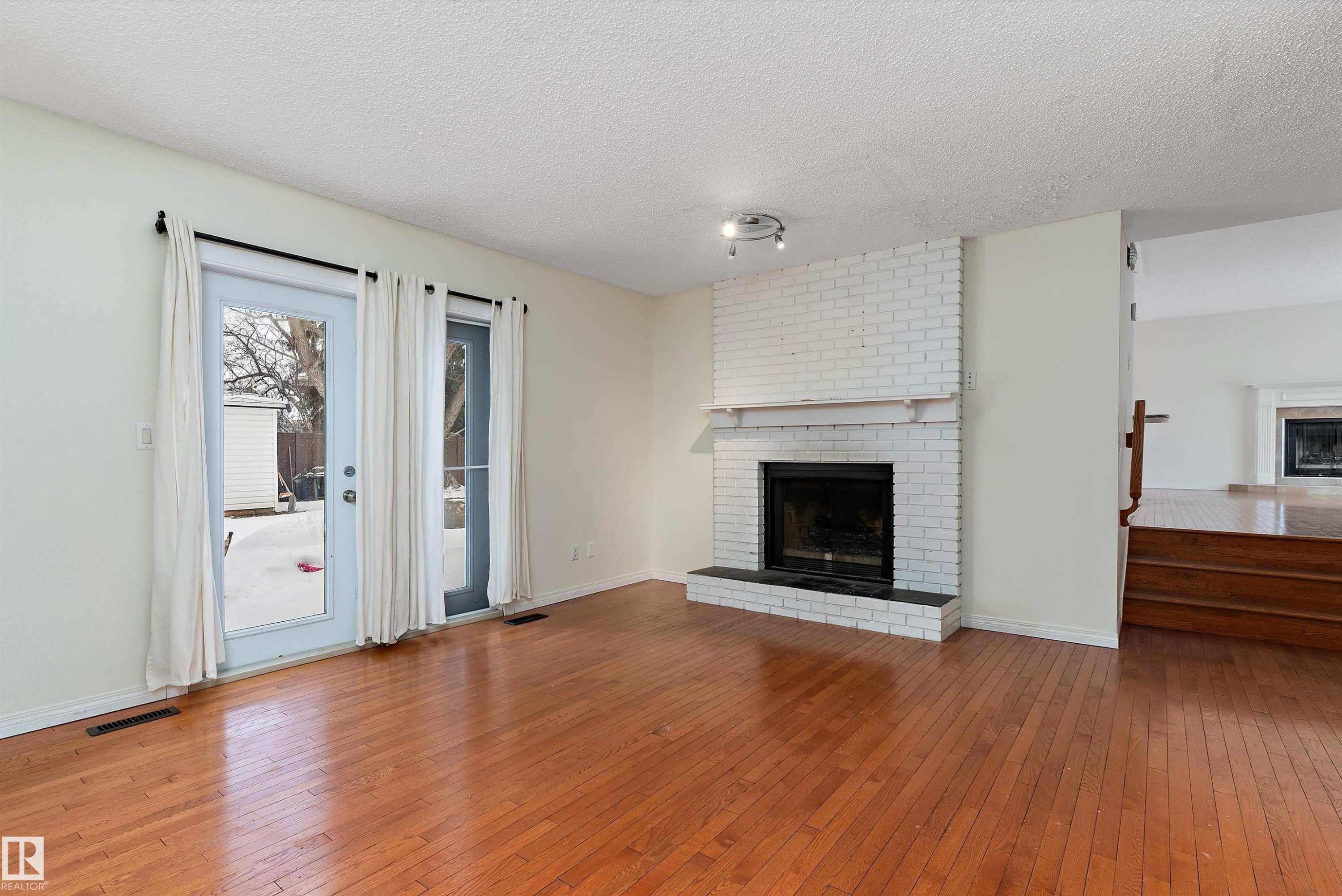 Unfurnished living room with a fireplace, hardwood / wood-style flooring, and a textured ceiling - 115 Walker Road, Edmonton, AB - Indoor Photo Showing Living Room With Fireplace