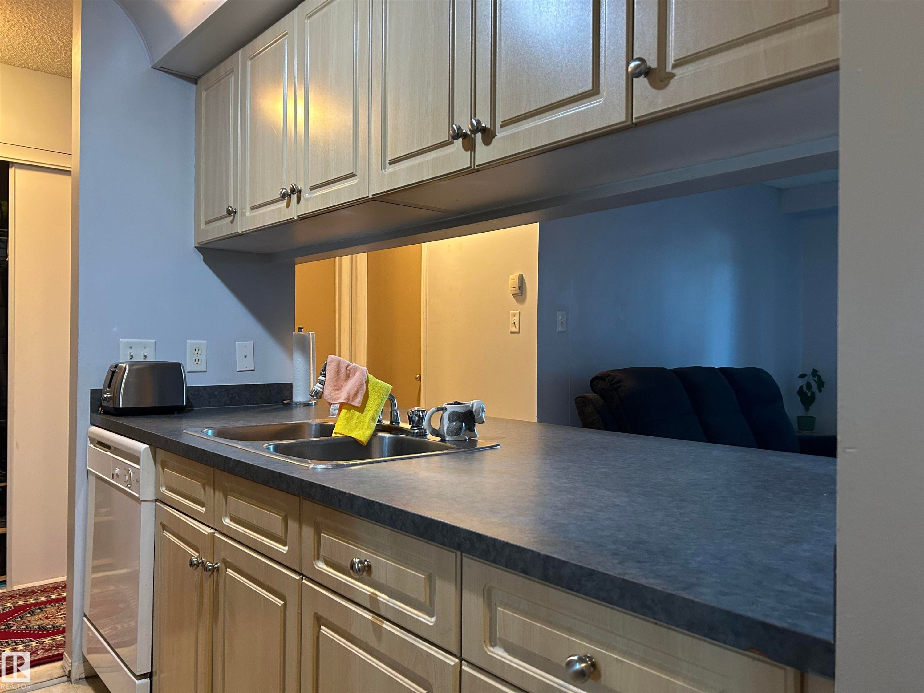 Kitchen featuring dark countertops and dishwasher - 310 2430 Guardian Road, Edmonton, AB - Indoor Photo Showing Kitchen With Double Sink