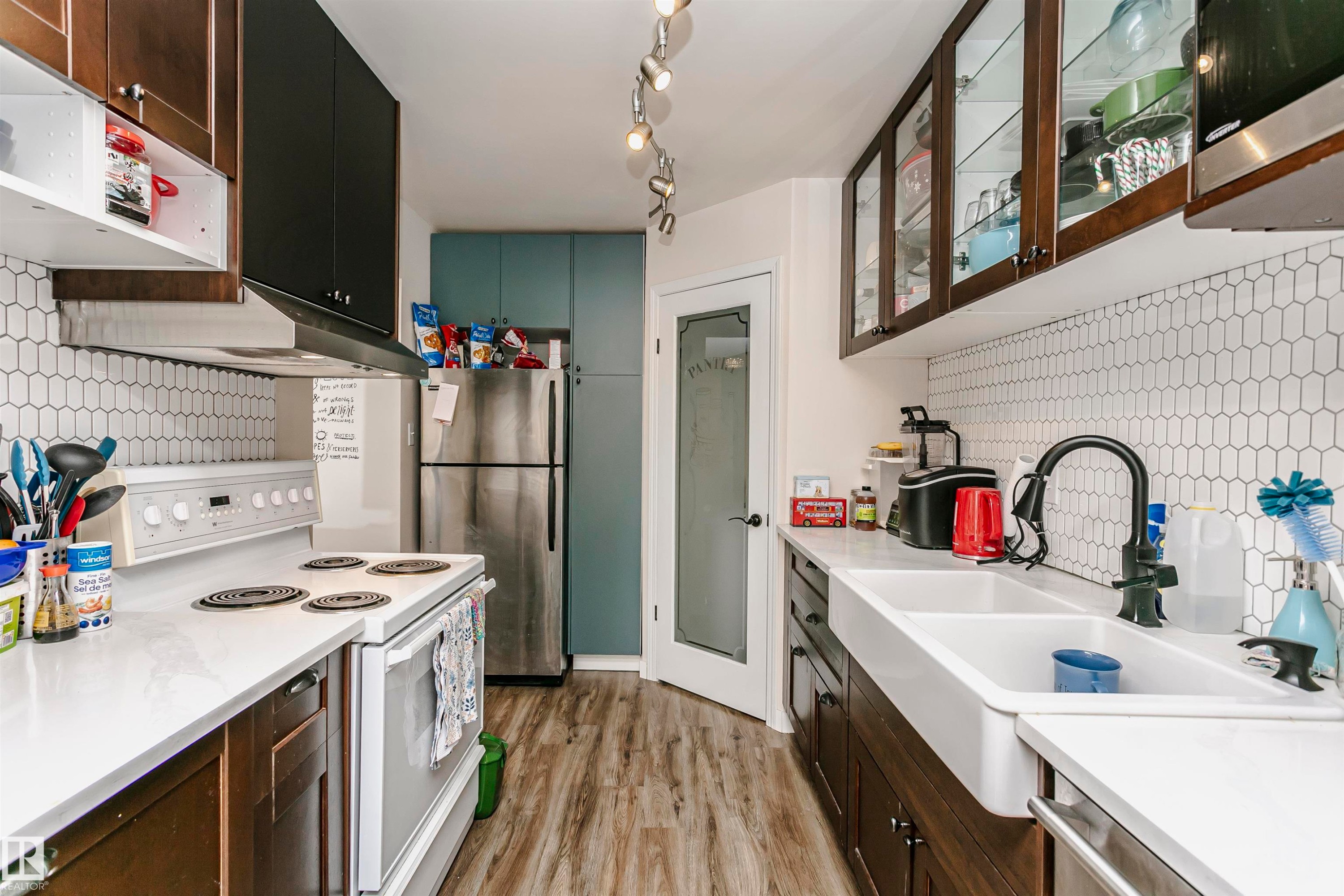 Kitchen with stainless steel appliances, decorative backsplash, glass insert cabinets, light wood finished floors, and two tone cabinetry - 407 8149 111 St S, Edmonton, AB - Indoor Photo Showing Kitchen