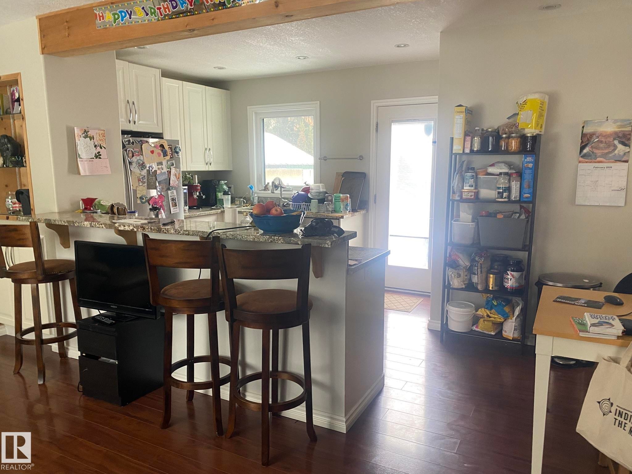 Kitchen with a breakfast bar, white cabinetry, freestanding refrigerator, dark wood finished floors, and a peninsula - 10945 54 Avenue, Edmonton, AB - Indoor Photo Showing Dining Room