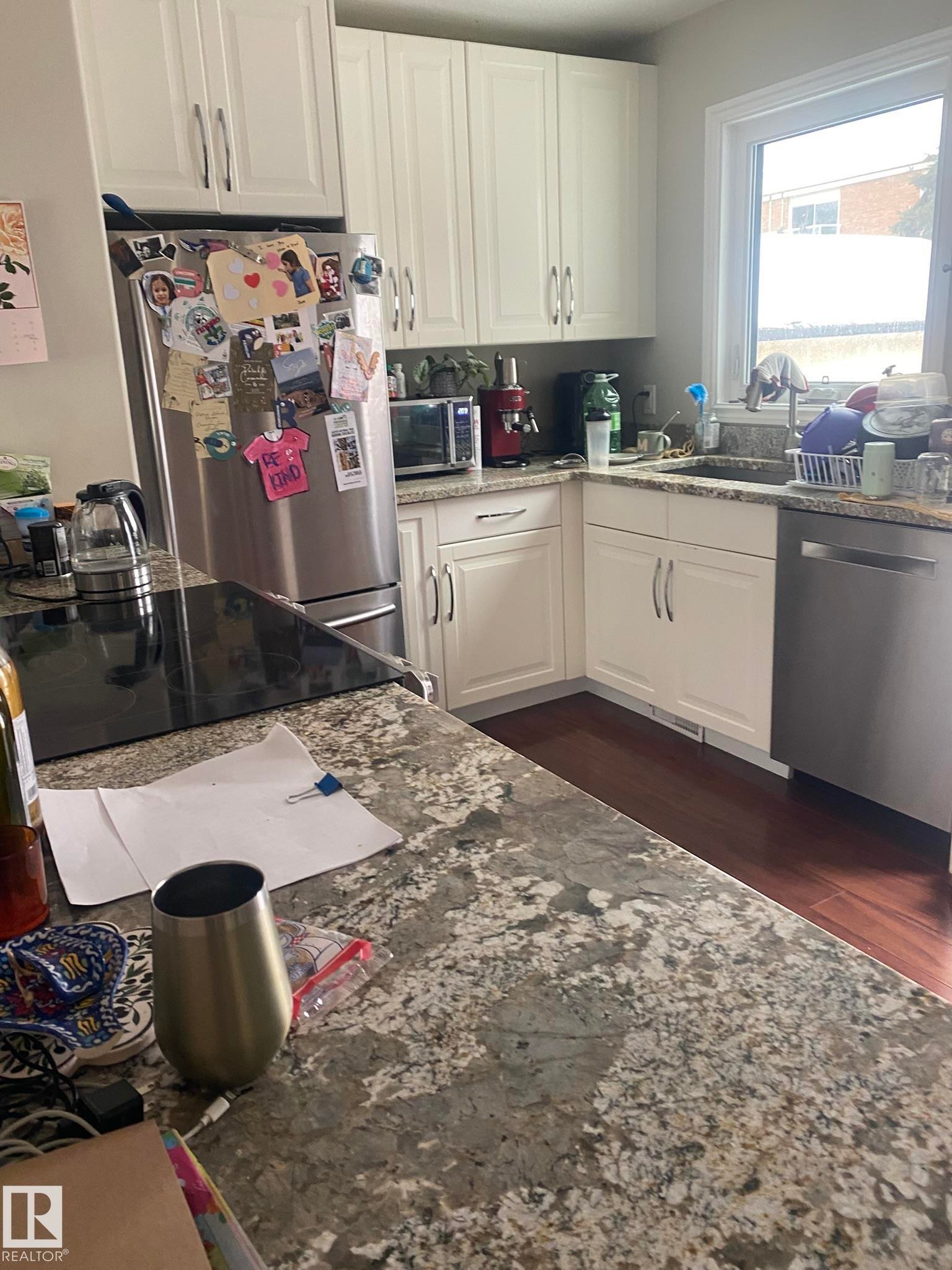 Kitchen featuring white cabinetry, stainless steel appliances, dark wood-style floors, and light stone counters - 10945 54 Avenue, Edmonton, AB - Indoor Photo Showing Kitchen