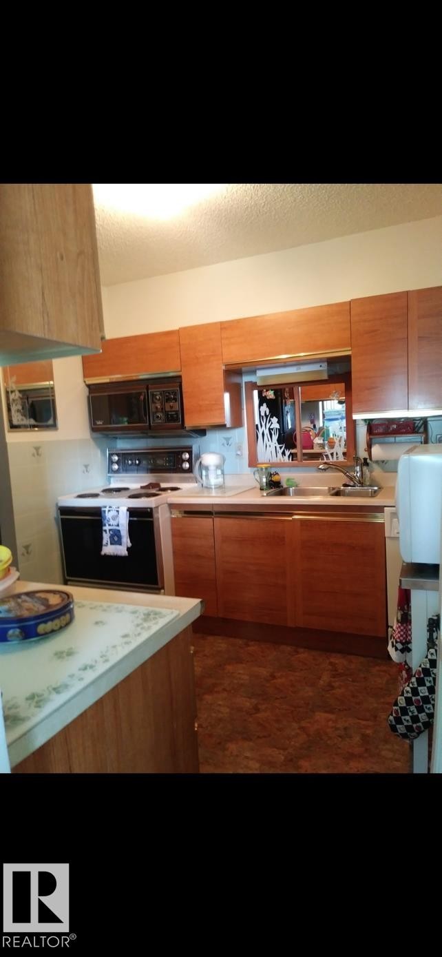 The kitchen features wood cabinetry, a built-in microwave, an oven range, and a double basin sink - 401 10743 107 Street Nw, Edmonton, AB - Indoor Photo Showing Kitchen
