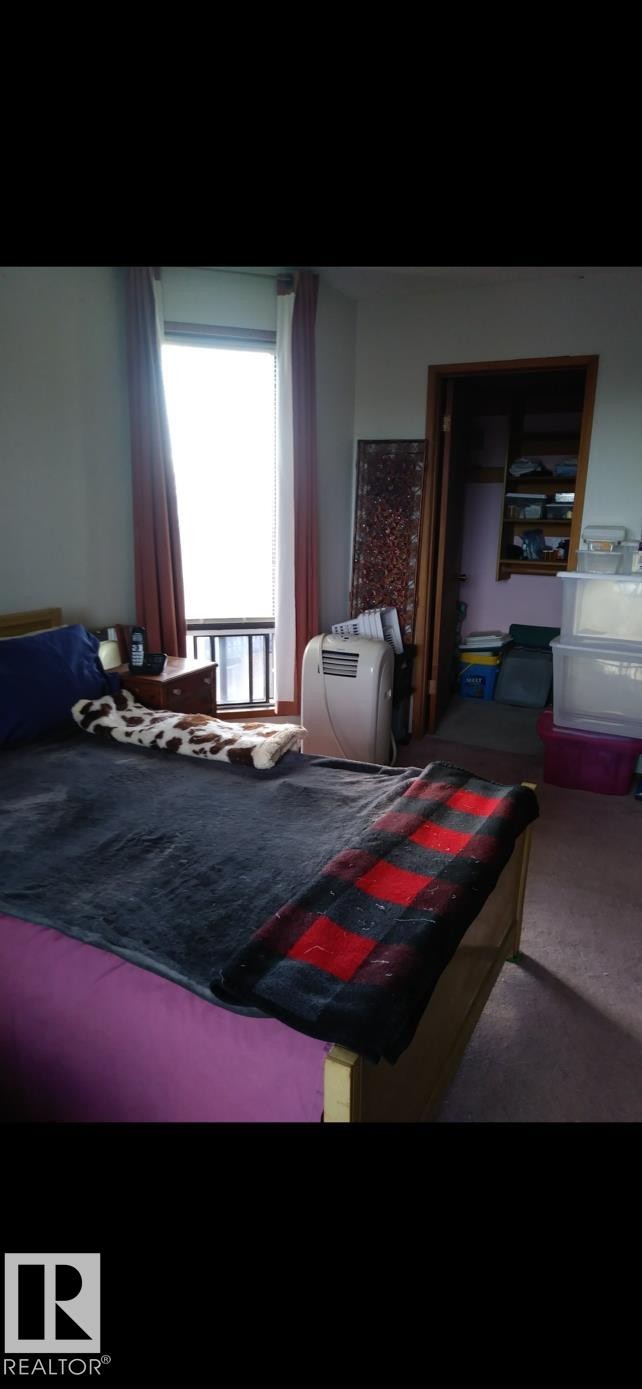 The room features a window with blinds and curtains, a wooden bed frame, and a closet with shelving - 401 10743 107 Street Nw, Edmonton, AB - Indoor Photo Showing Bedroom