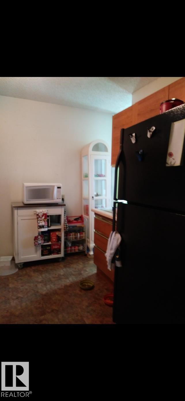 The kitchen features a black refrigerator, wood cabinetry, and a white display cabinet - 401 10743 107 Street Nw, Edmonton, AB - Indoor