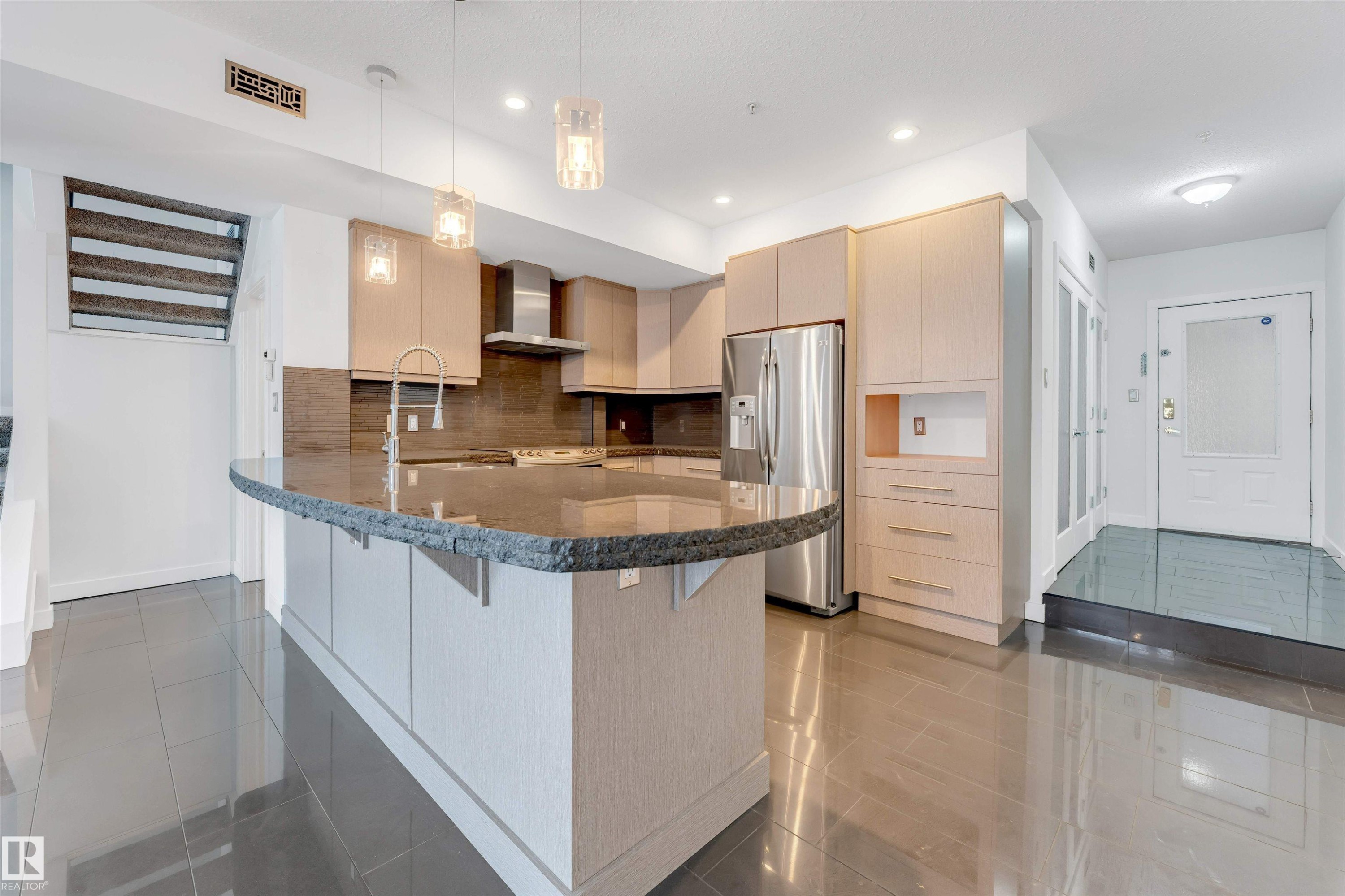 Kitchen with light wood finish cabinetry, stainless steel refrigerator with ice dispenser, a peninsula, pendant lighting, and a breakfast bar - 102 10711 83 Avenue, Edmonton, AB - Indoor Photo Showing Kitchen With Stainless Steel Kitchen With Upgraded Kitchen