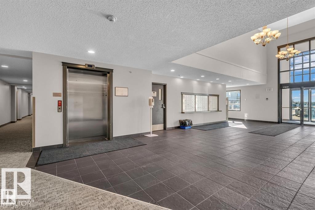 The property features a spacious lobby with tile flooring, a stainless steel elevator, and large windows that provide natural light - 3309 9351 Simpson Drive, Edmonton, AB - Indoor Photo Showing Other Room