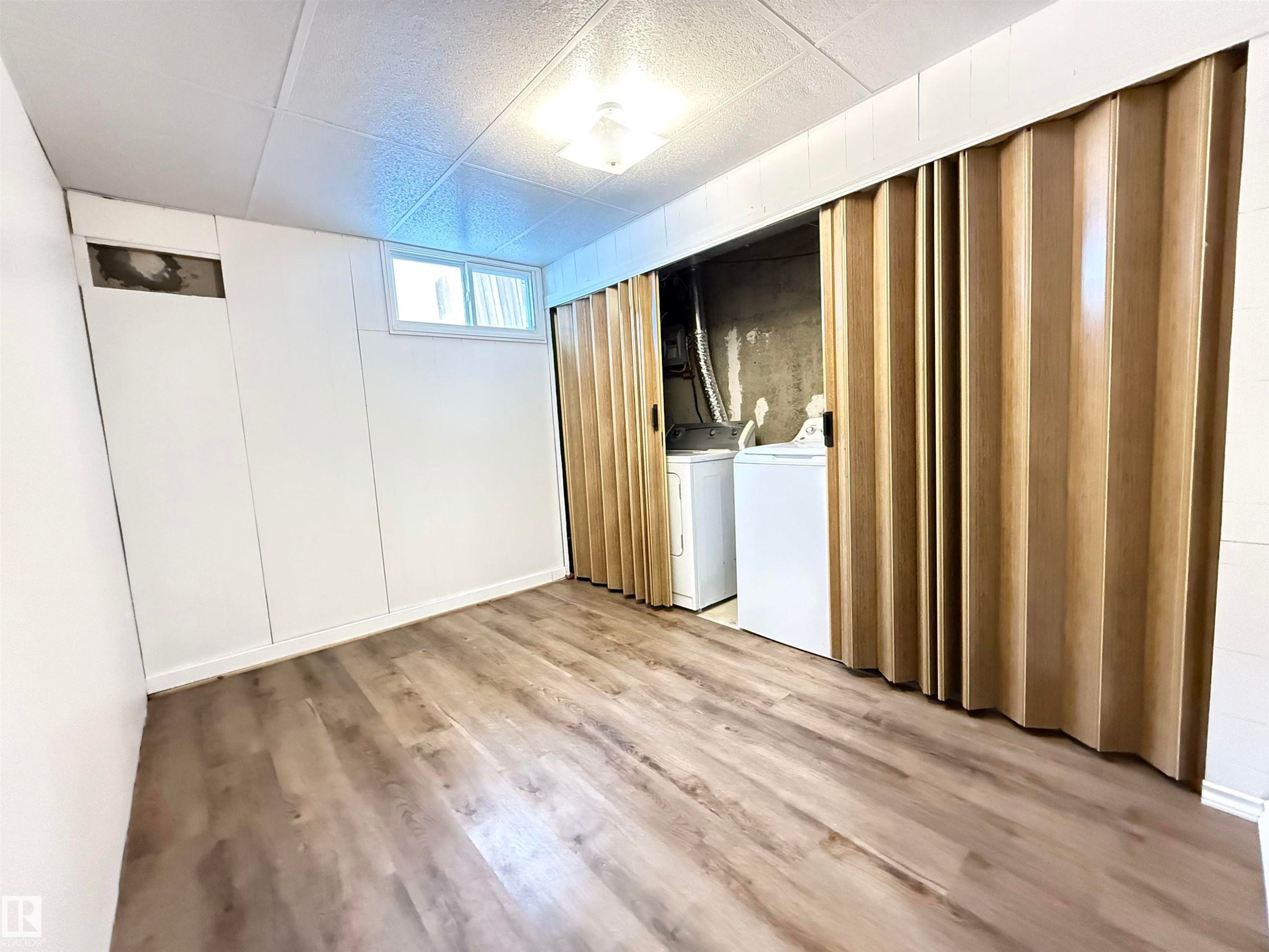 Below grade area with light wood-style floors, washer and dryer, and a drop ceiling - 9034 60 Street, Edmonton, AB - Indoor Photo Showing Other Room