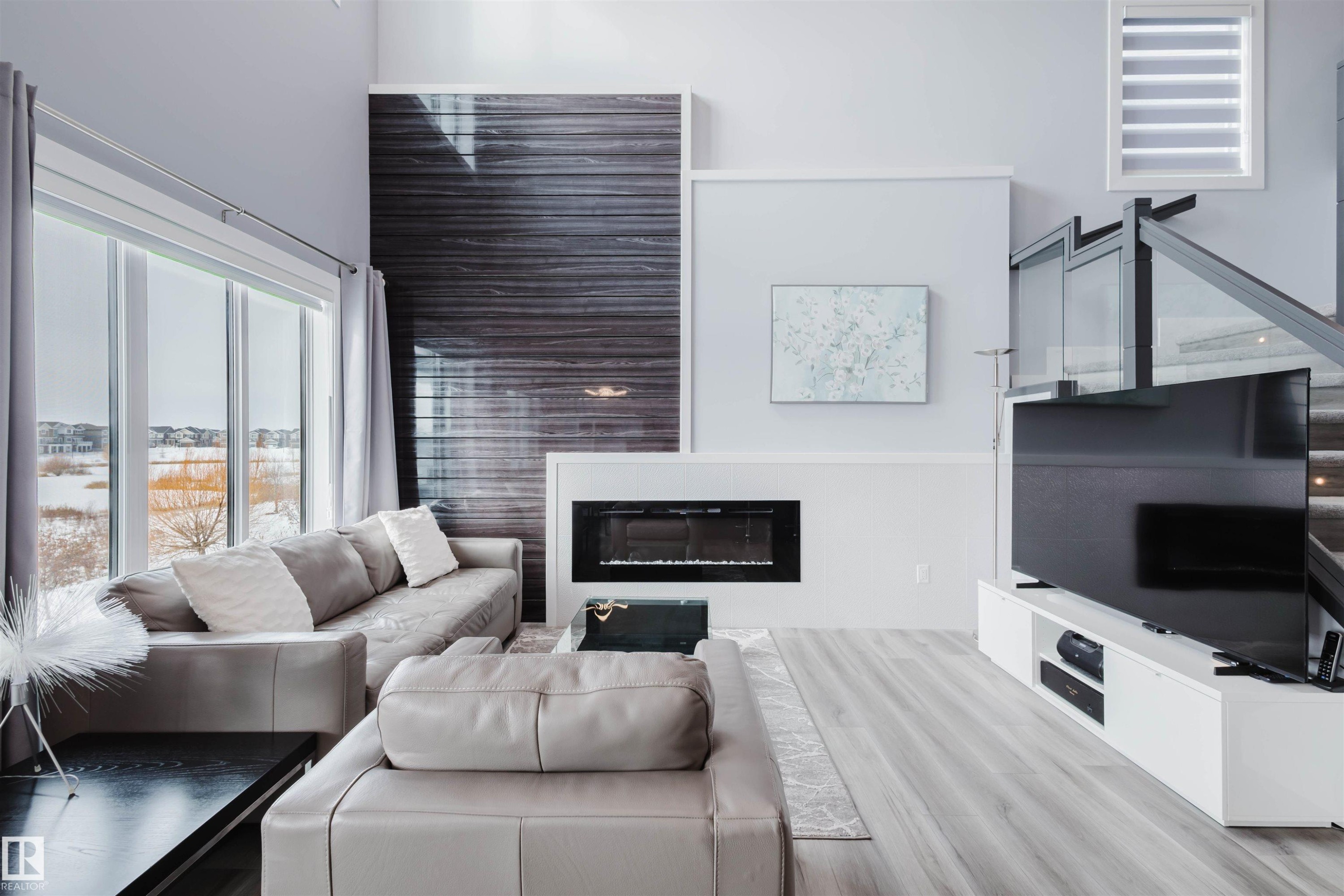 Living area with a glass covered fireplace, light wood finished floors, and a high ceiling - 16217 32 Avenue, Edmonton, AB - Indoor Photo Showing Living Room With Fireplace