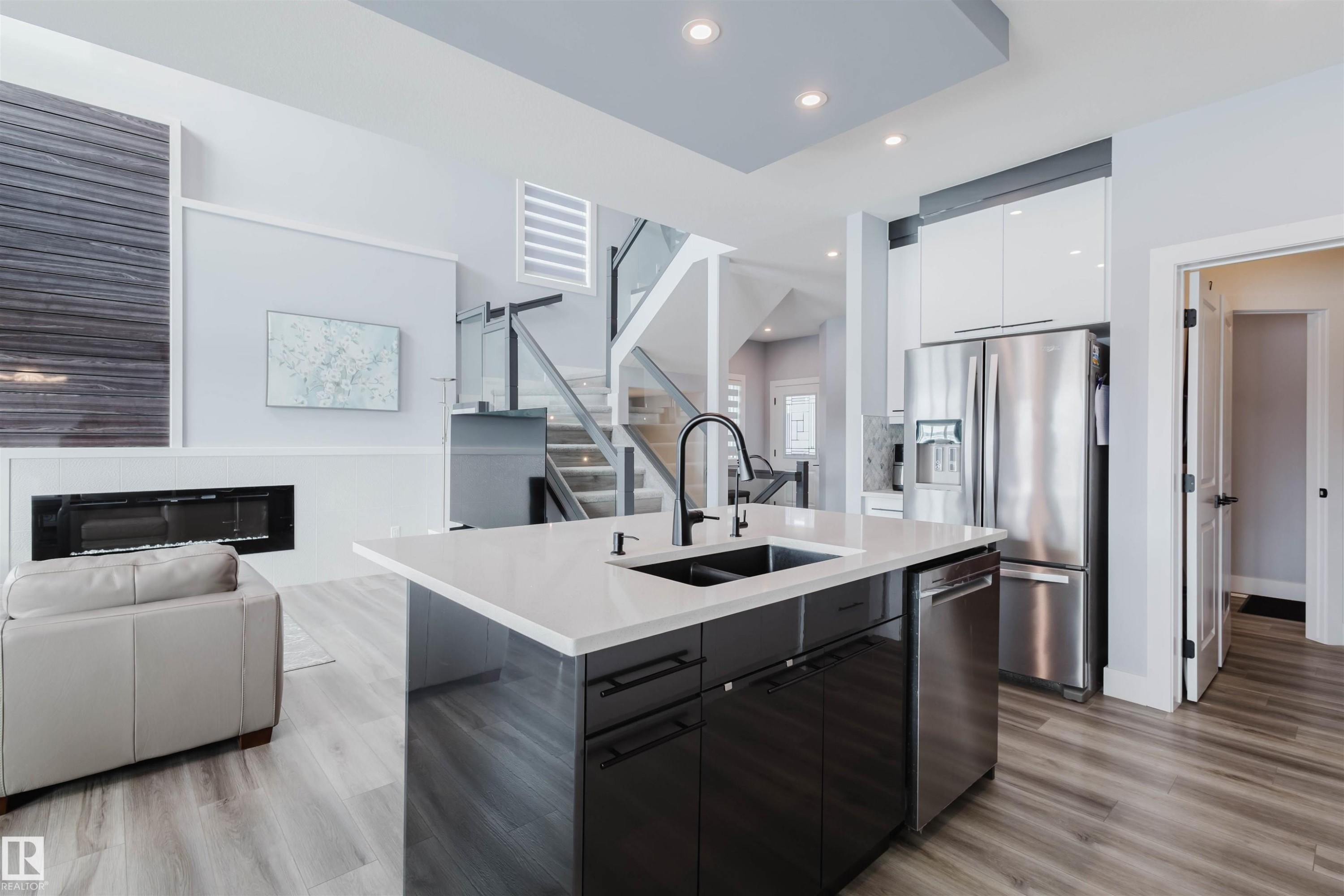 Kitchen featuring modern cabinets, open floor plan, stainless steel appliances, an island with sink, and a glass covered fireplace - 16217 32 Avenue, Edmonton, AB - Indoor Photo Showing Kitchen With Double Sink With Upgraded Kitchen