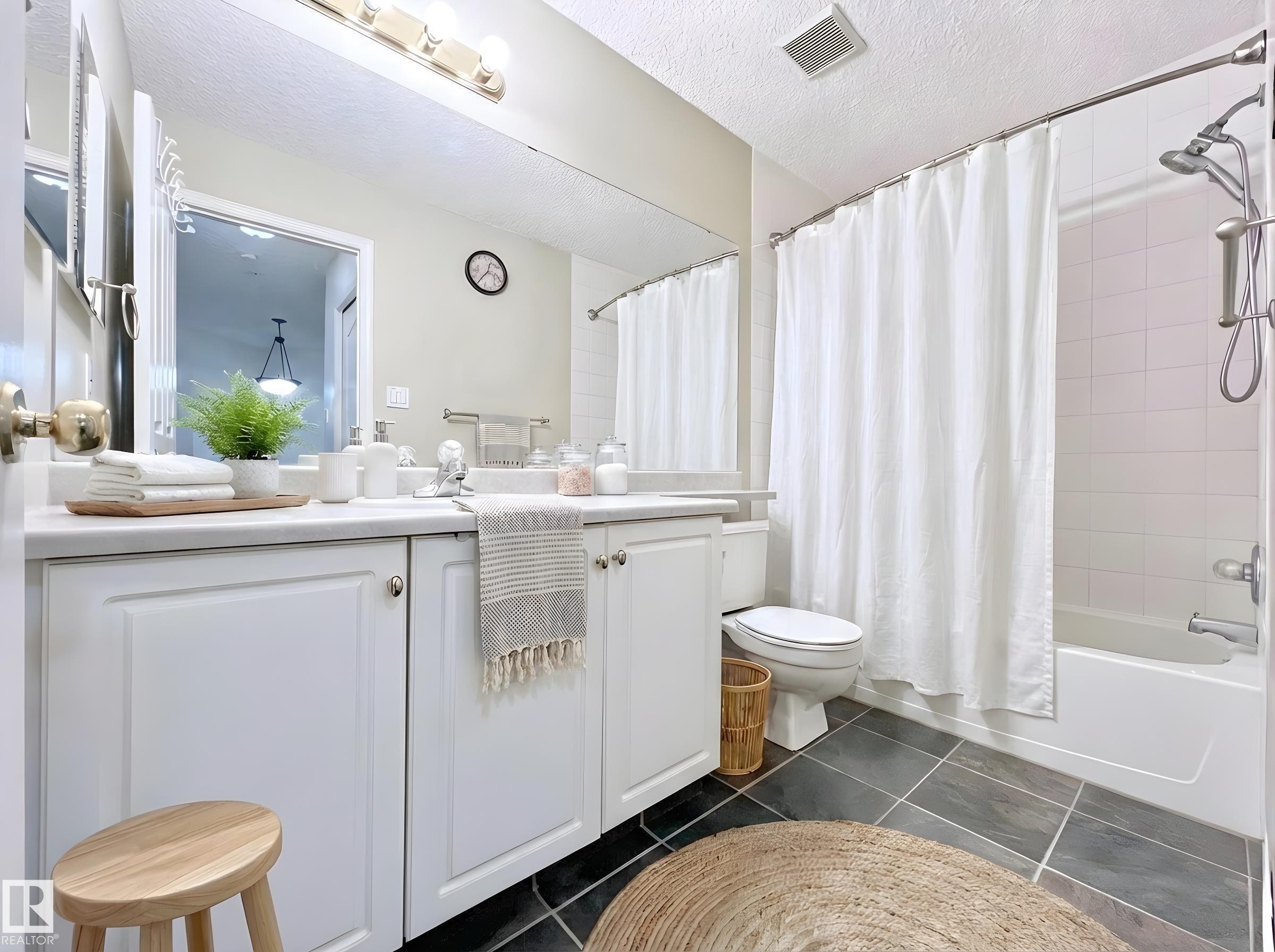 Bathroom featuring vanity, shower / tub combo with curtain, dark tile patterned flooring, and a textured ceiling - 110 10511 42 Avenue, Edmonton, AB - Indoor Photo Showing Bathroom