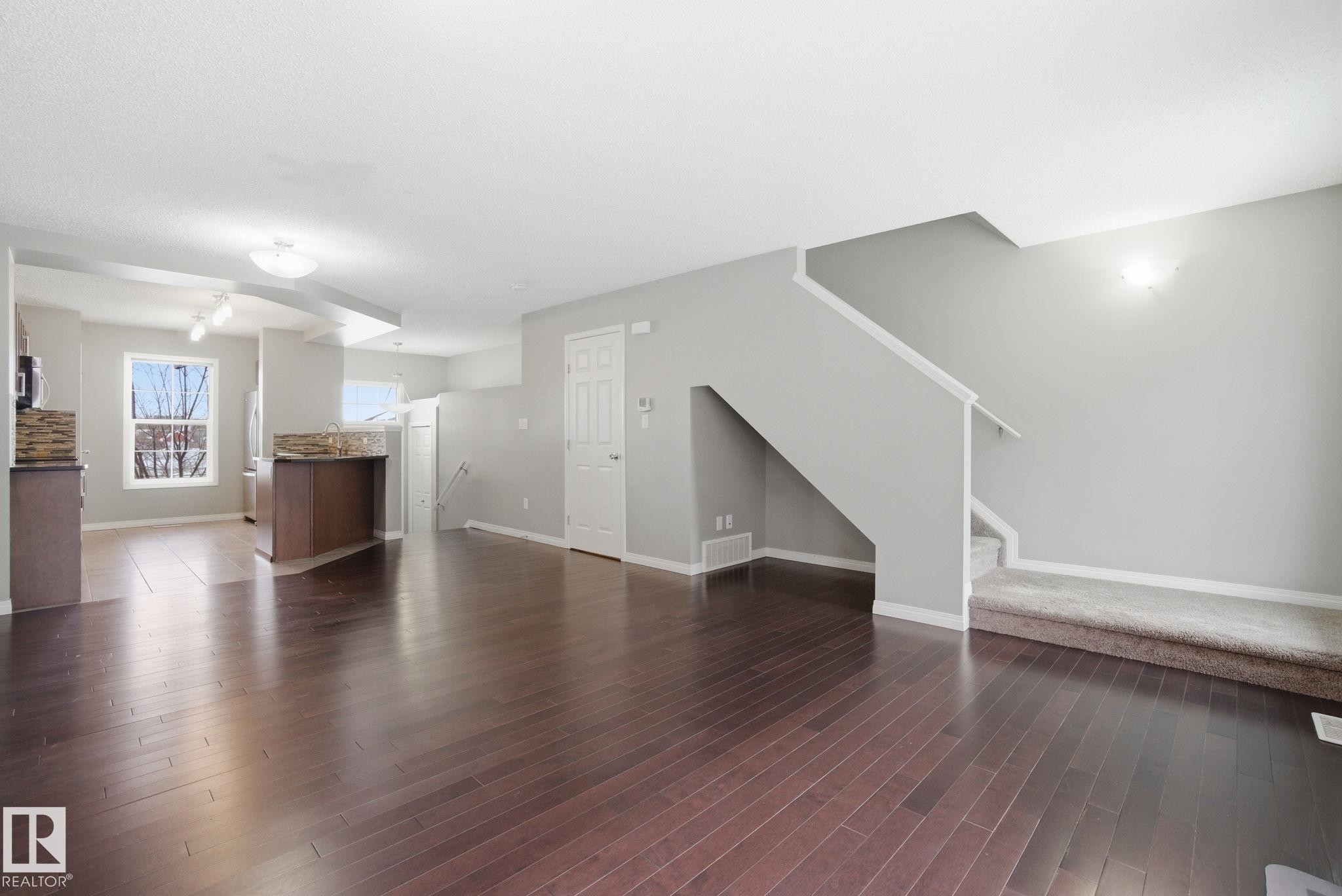 Unfurnished living room with stairs and dark wood-style flooring - 71 4029 Orchards Drive, Edmonton, AB - Indoor Photo Showing Living Room
