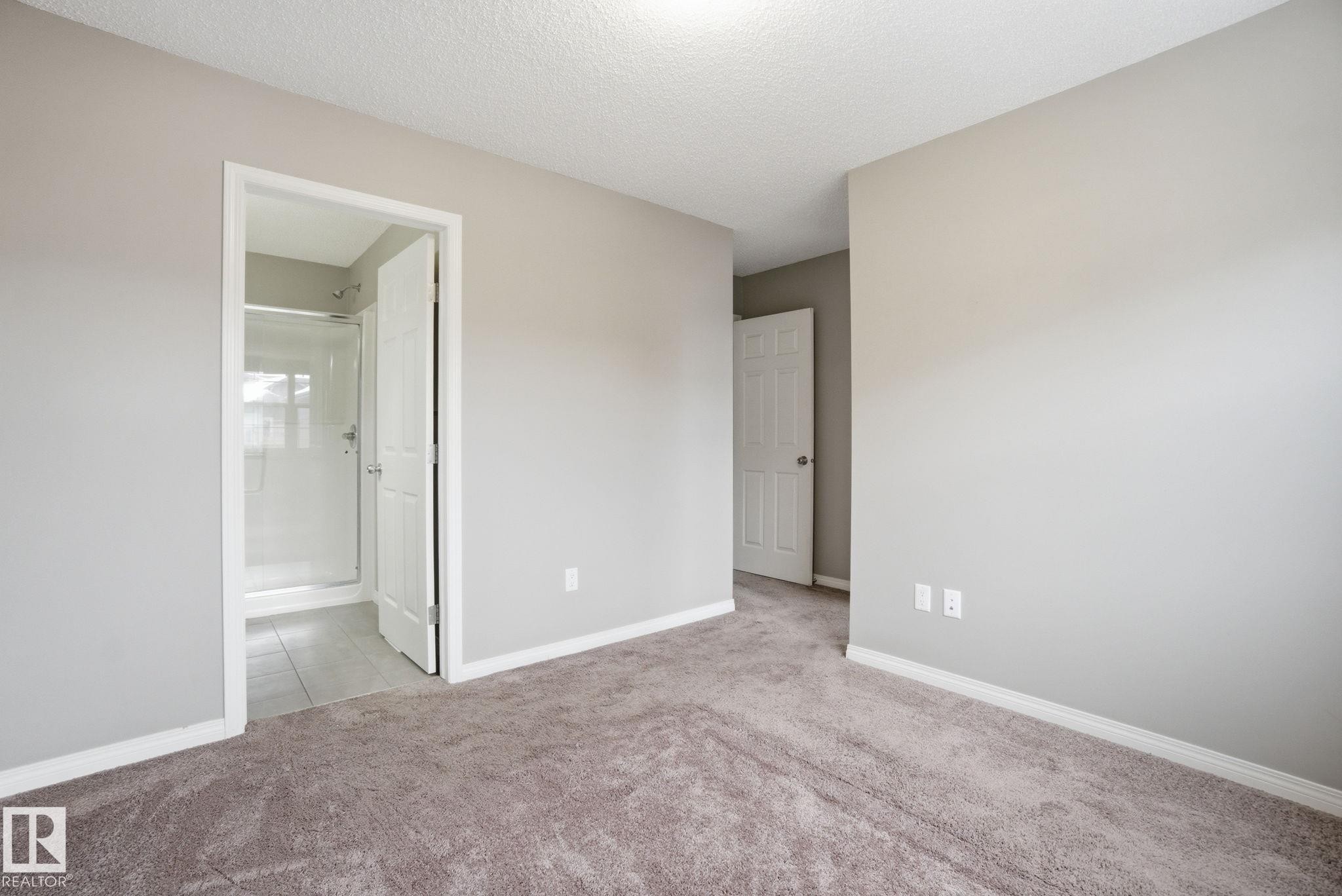 Unfurnished bedroom featuring light colored carpet, a textured ceiling, and ensuite bathroom - 71 4029 Orchards Drive, Edmonton, AB - Indoor Photo Showing Other Room