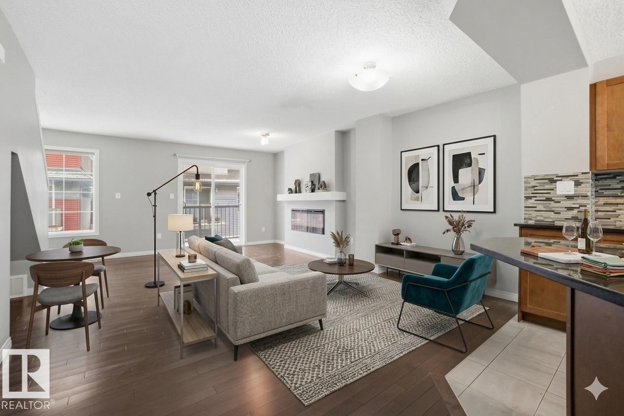 Living area featuring dark wood-type flooring, a textured ceiling, and a glass covered fireplace - 71 4029 Orchards Drive, Edmonton, AB - Indoor Photo Showing Living Room With Fireplace