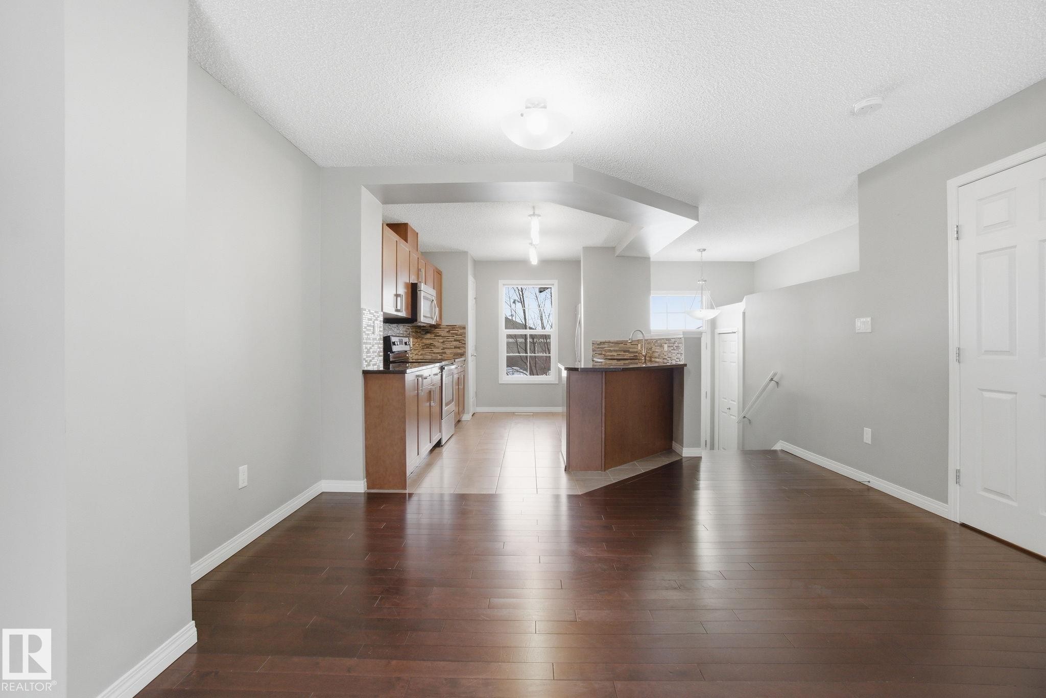 Unfurnished living room featuring dark wood-type flooring and a textured ceiling - 71 4029 Orchards Drive, Edmonton, AB - Indoor