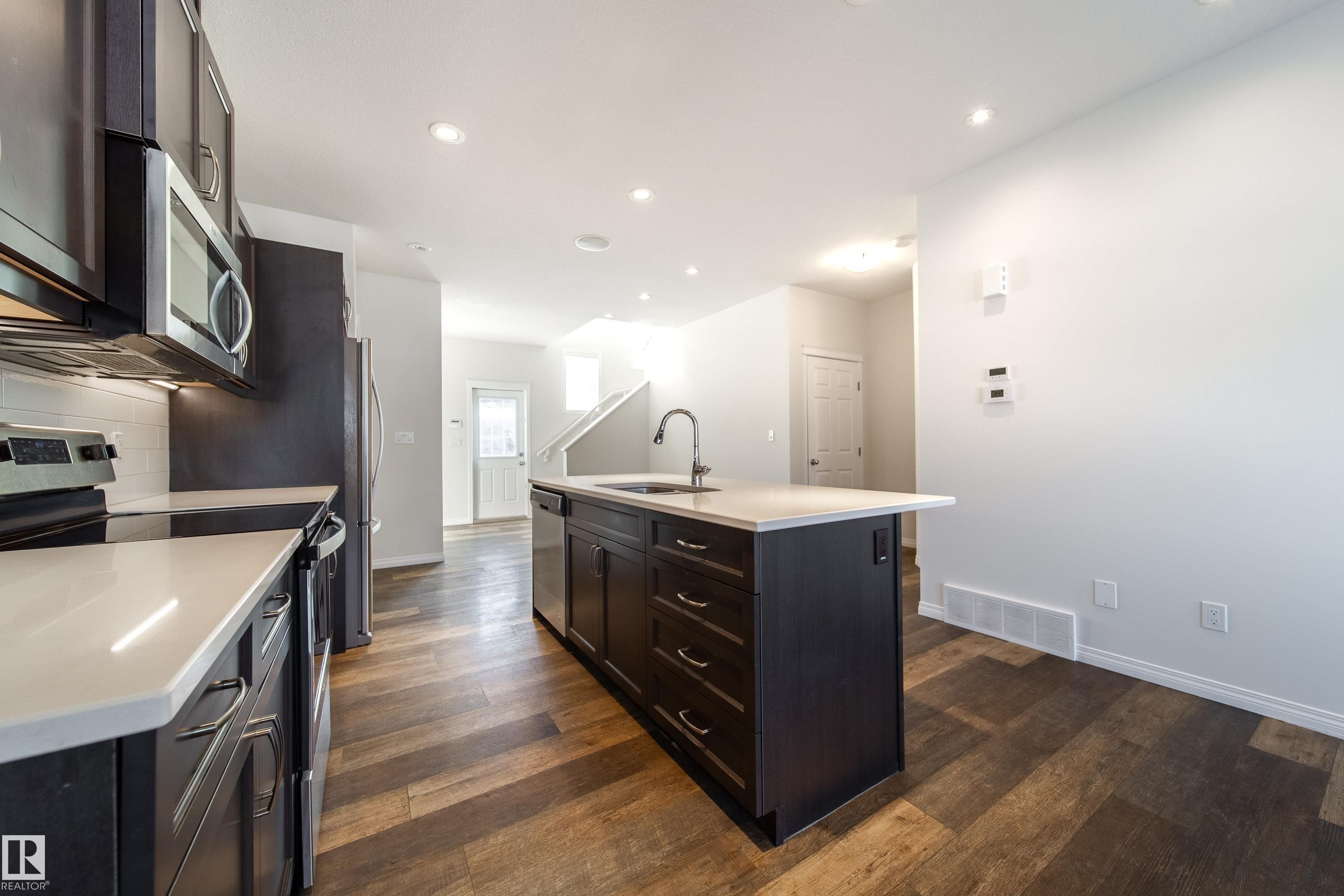 Kitchen featuring stainless steel appliances, an island with sink, dark wood-type flooring, recessed lighting, and dark wood finish cabinets - 1199 Watt Drive, Edmonton, AB - Indoor Photo Showing Kitchen With Upgraded Kitchen