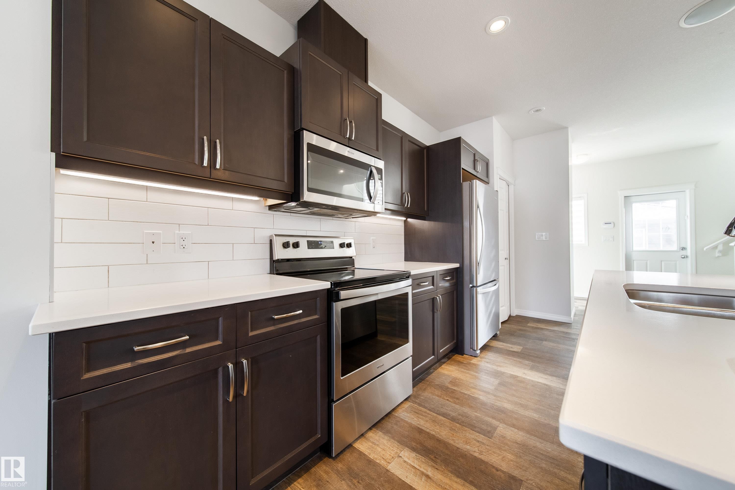 Kitchen featuring stainless steel appliances, dark wood finish cabinets, light wood-type flooring, decorative backsplash, and recessed lighting - 1199 Watt Drive, Edmonton, AB - Indoor Photo Showing Kitchen With Double Sink With Upgraded Kitchen