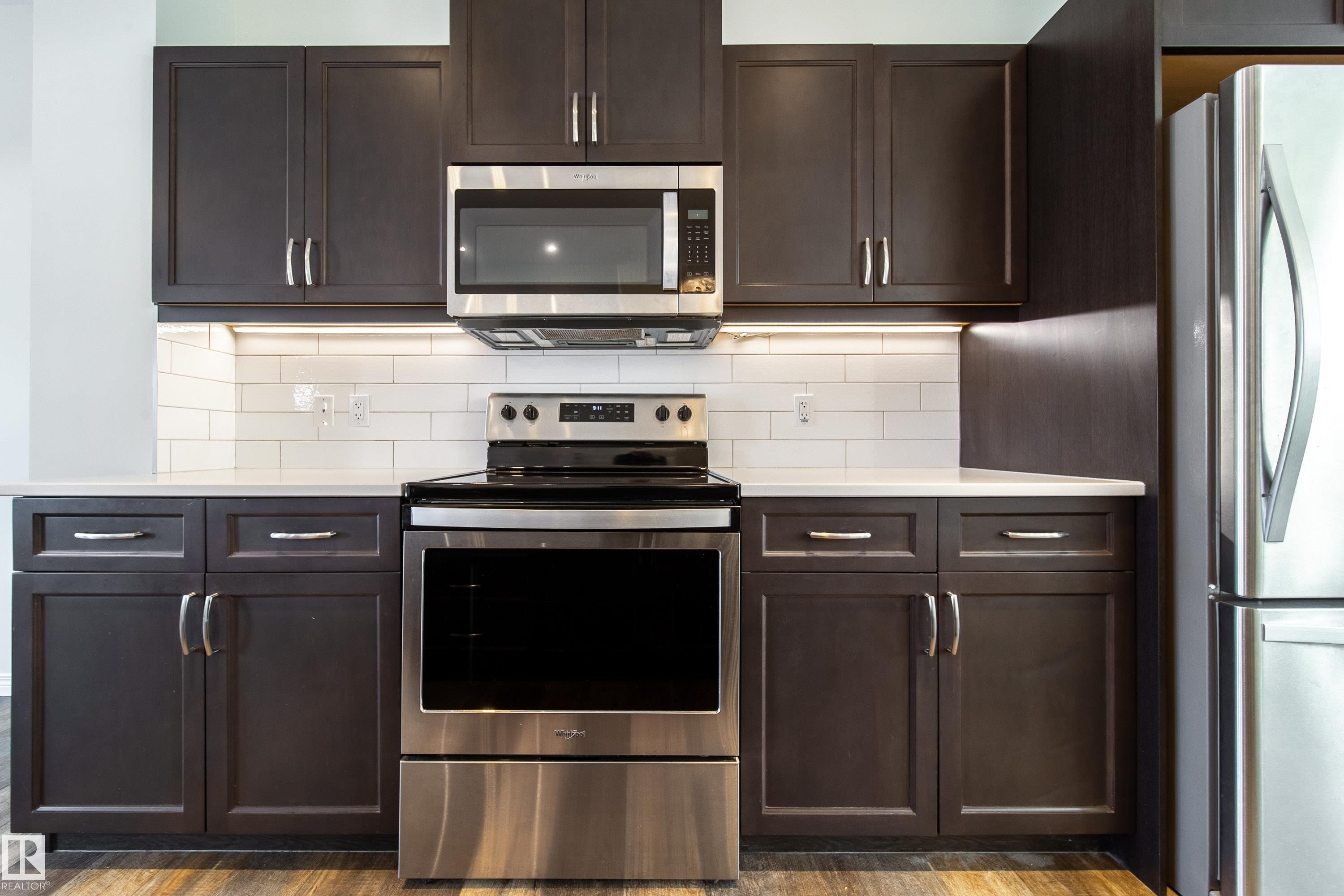 Kitchen featuring stainless steel appliances, dark wood finish cabinets, tasteful backsplash, light stone counters, and dark wood finished floors - 1199 Watt Drive, Edmonton, AB - Indoor Photo Showing Kitchen