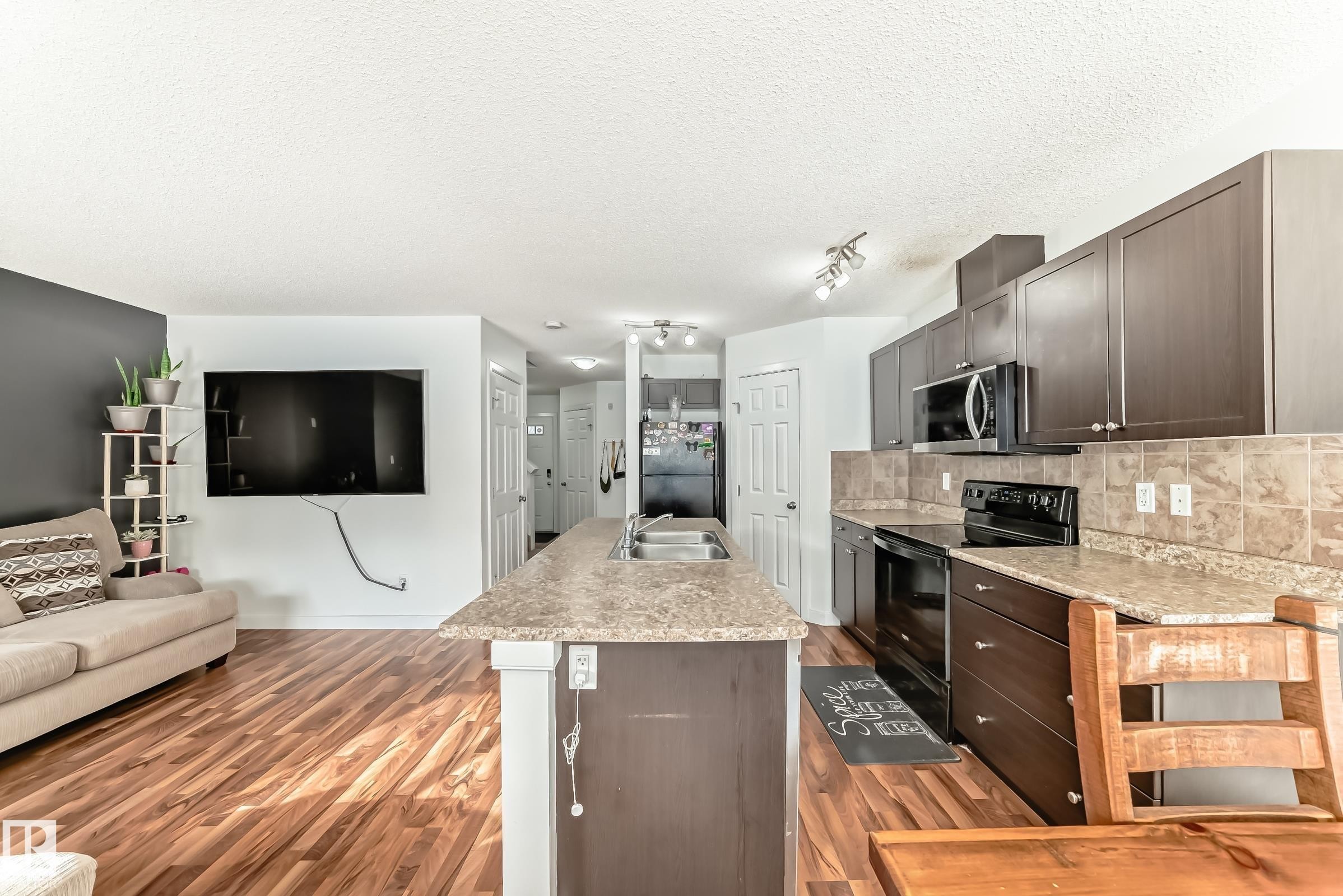 Kitchen with black appliances, open floor plan, a center island with sink, light countertops, and tasteful backsplash - 17357 8A Avenue, Edmonton, AB