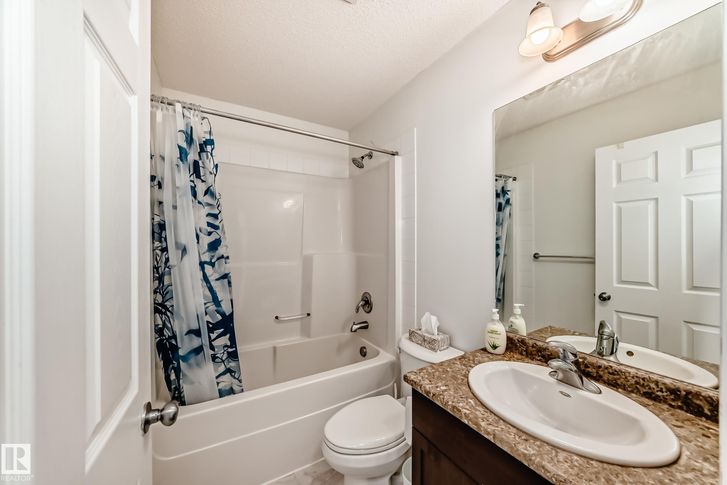 Bathroom featuring vanity, shower / bathtub combination with curtain, and a textured ceiling - 17357 8A Avenue, Edmonton, AB