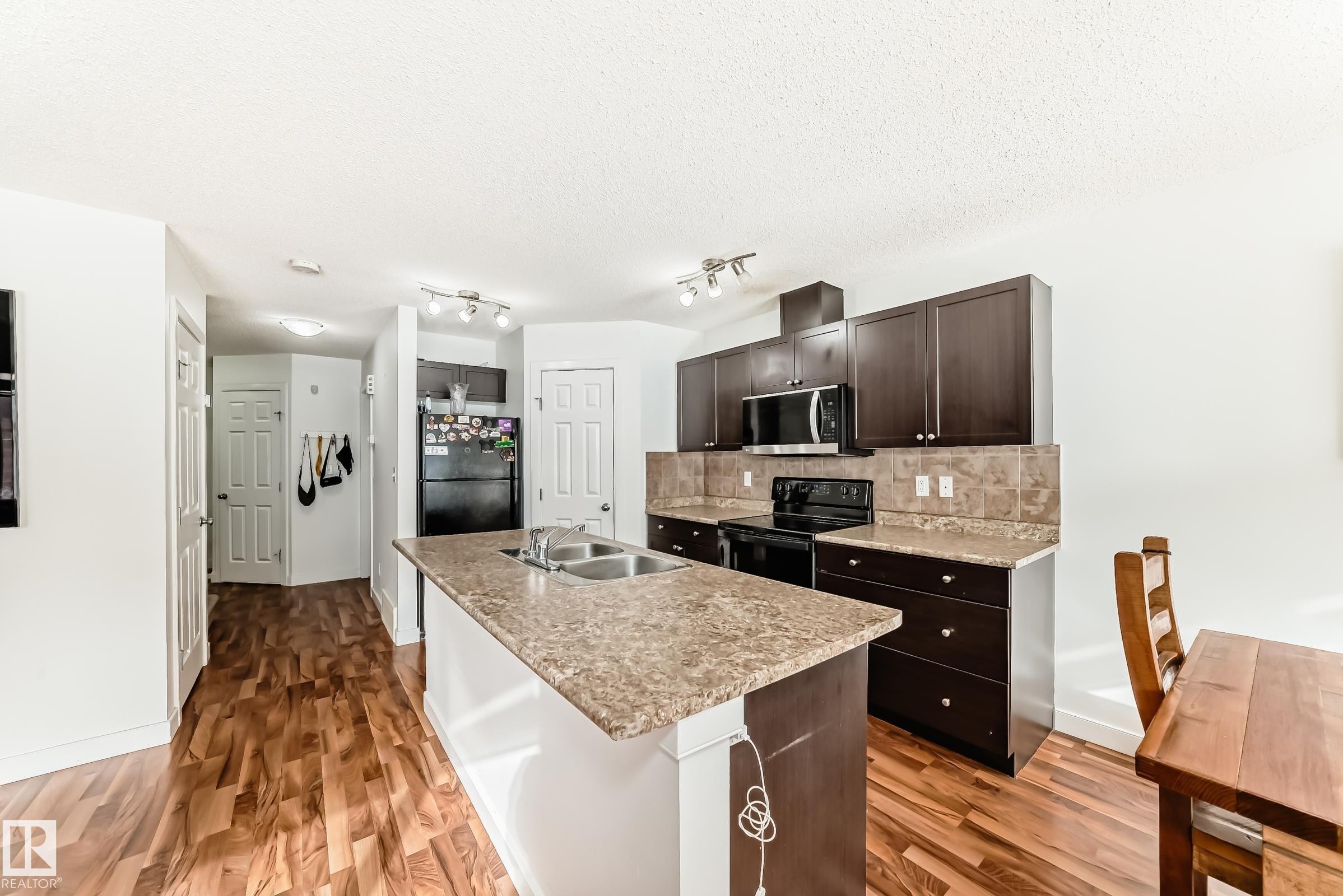 Kitchen featuring light countertops, black appliances, backsplash, dark wood finish cabinets, and a center island with sink - 17357 8A Avenue, Edmonton, AB