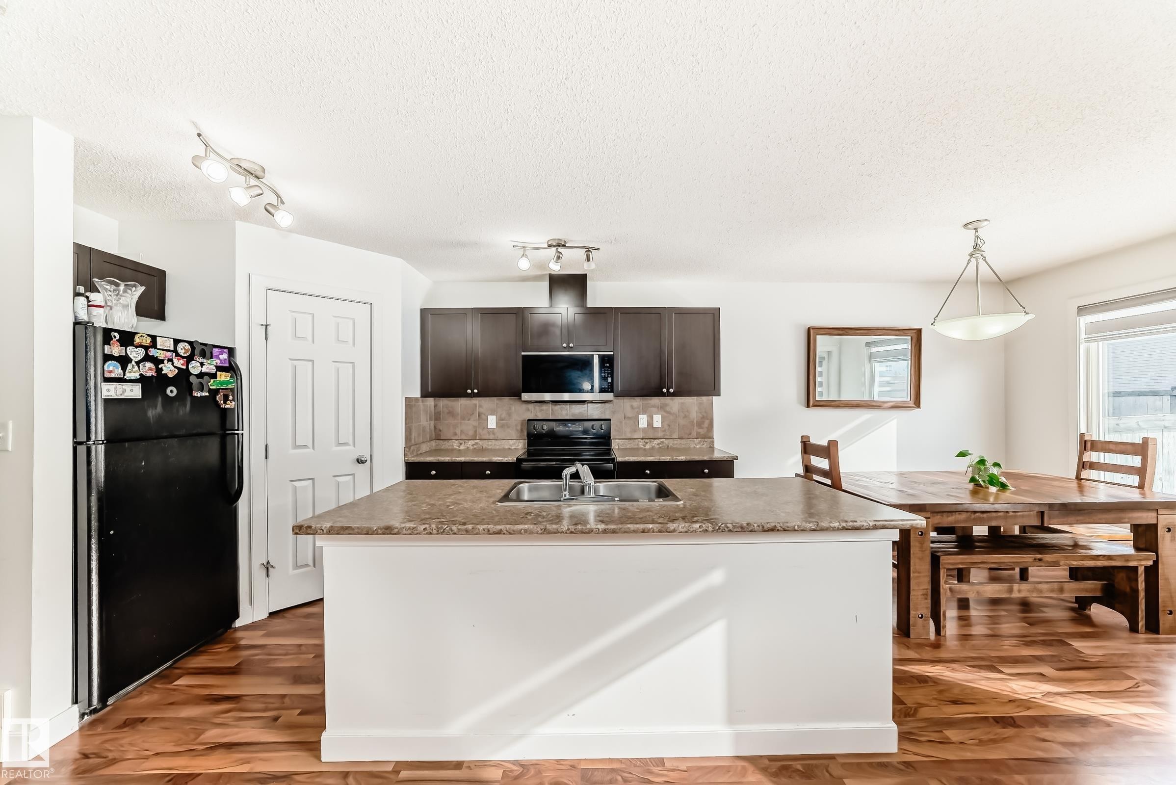 Kitchen featuring black appliances, decorative backsplash, a center island with sink, dark wood finished floors, and dark wood finish cabinetry - 17357 8A Avenue, Edmonton, AB