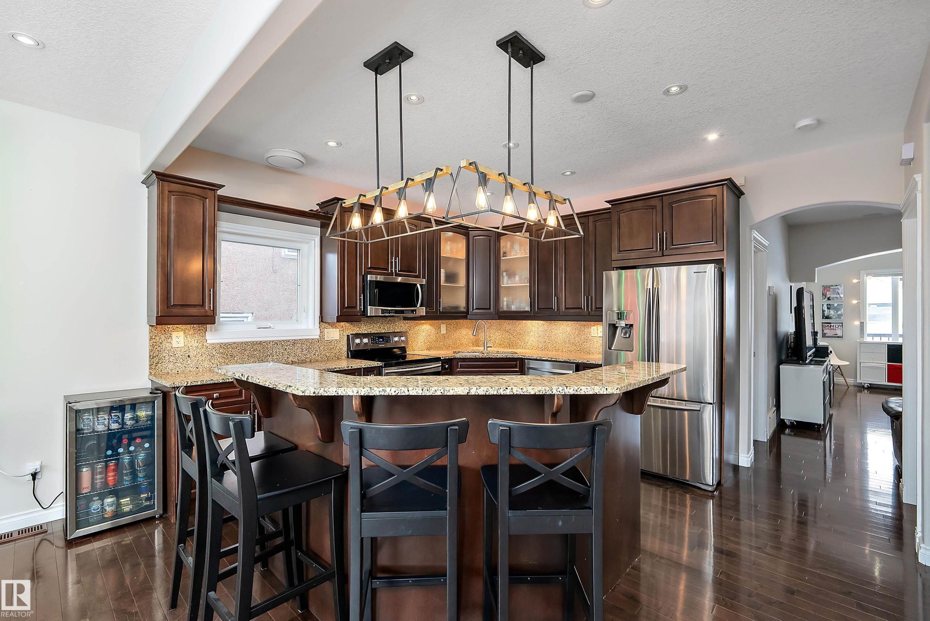 Kitchen featuring arched walkways, dark wood finish cabinets, glass fronted cabinets, stainless steel appliances, and a kitchen bar - 10623 75 Avenue, Edmonton, AB - Indoor