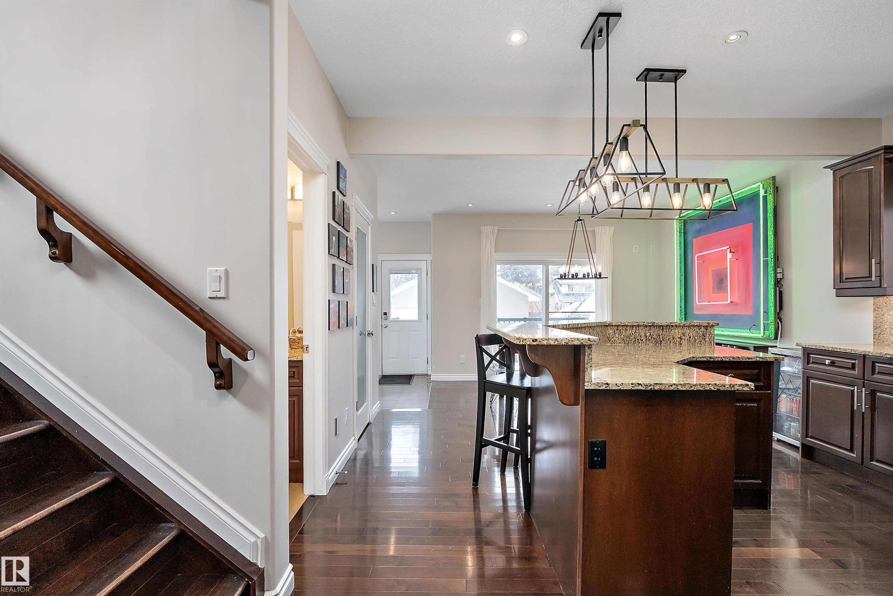 Kitchen featuring dark wood finish cabinets, a kitchen island, light stone counters, pendant lighting, and a kitchen bar - 10623 75 Avenue, Edmonton, AB - Indoor