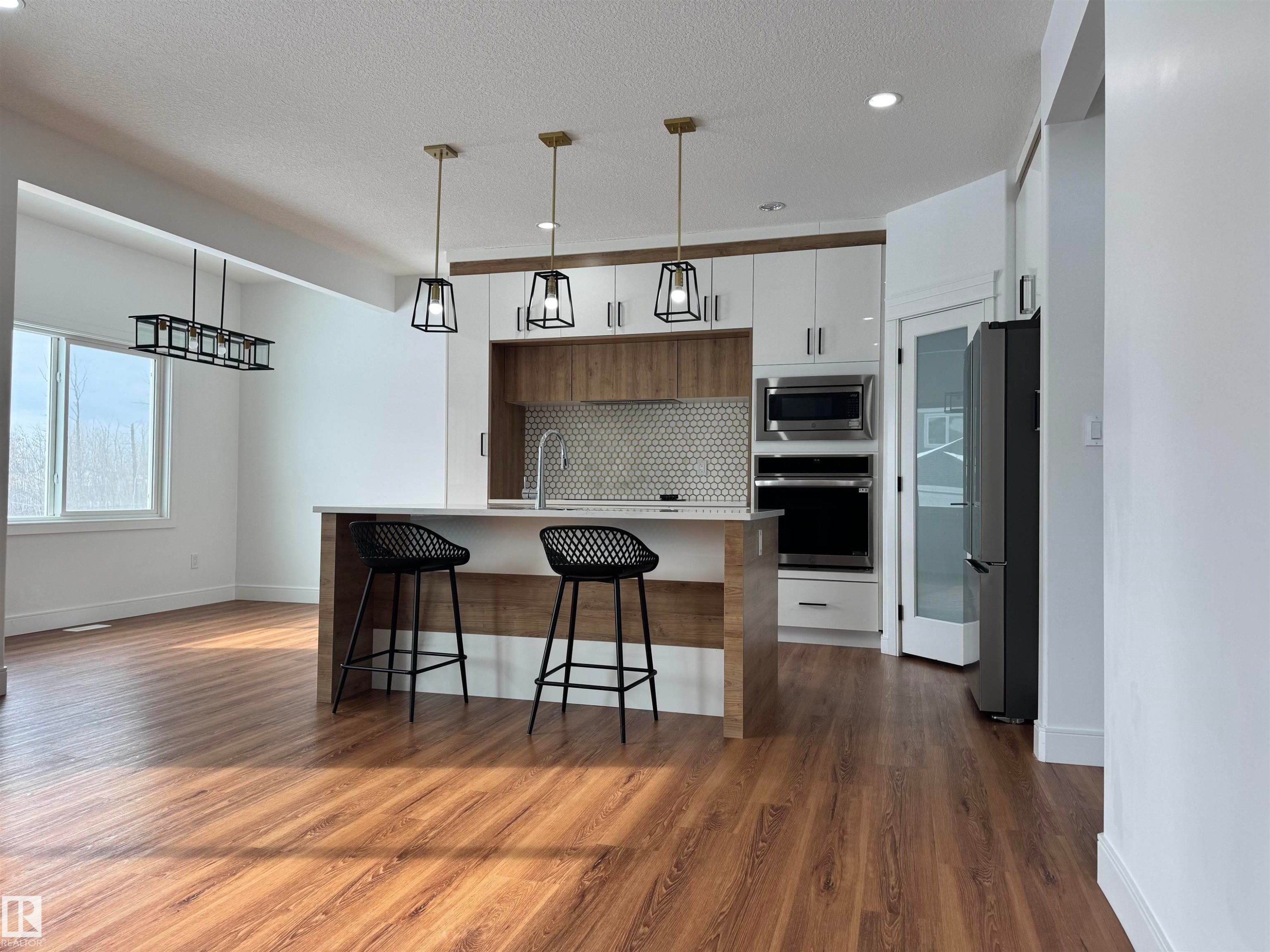 Kitchen with modern cabinets, stainless steel appliances, a breakfast bar area, a center island with sink, and decorative light fixtures - 1703 152 Avenue, Edmonton, AB - Indoor Photo Showing Kitchen