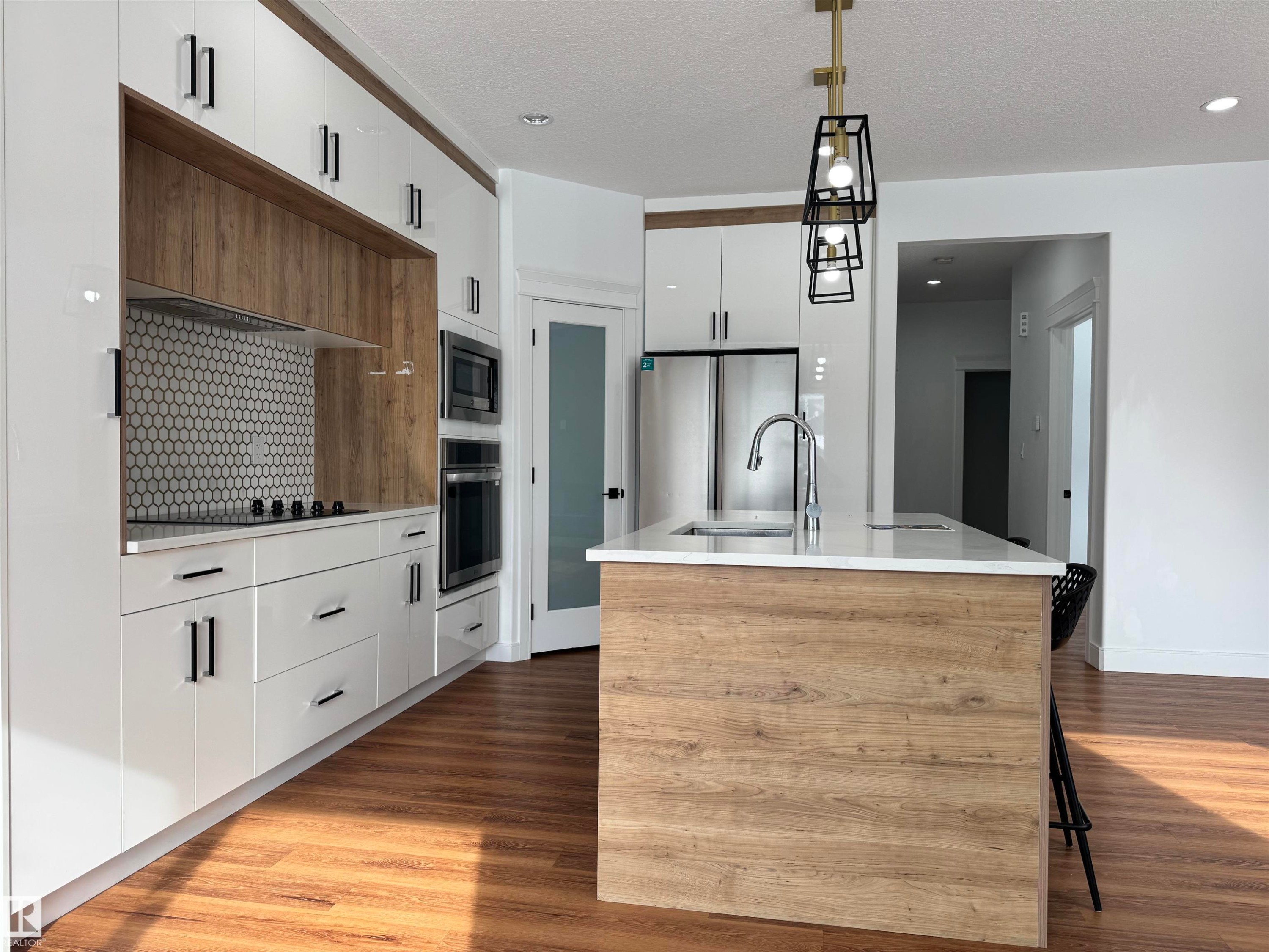 Kitchen with two tone color scheme, an island with sink, dark wood-style floors, a kitchen bar, and decorative light fixtures - 1703 152 Avenue, Edmonton, AB - Indoor Photo Showing Kitchen With Upgraded Kitchen