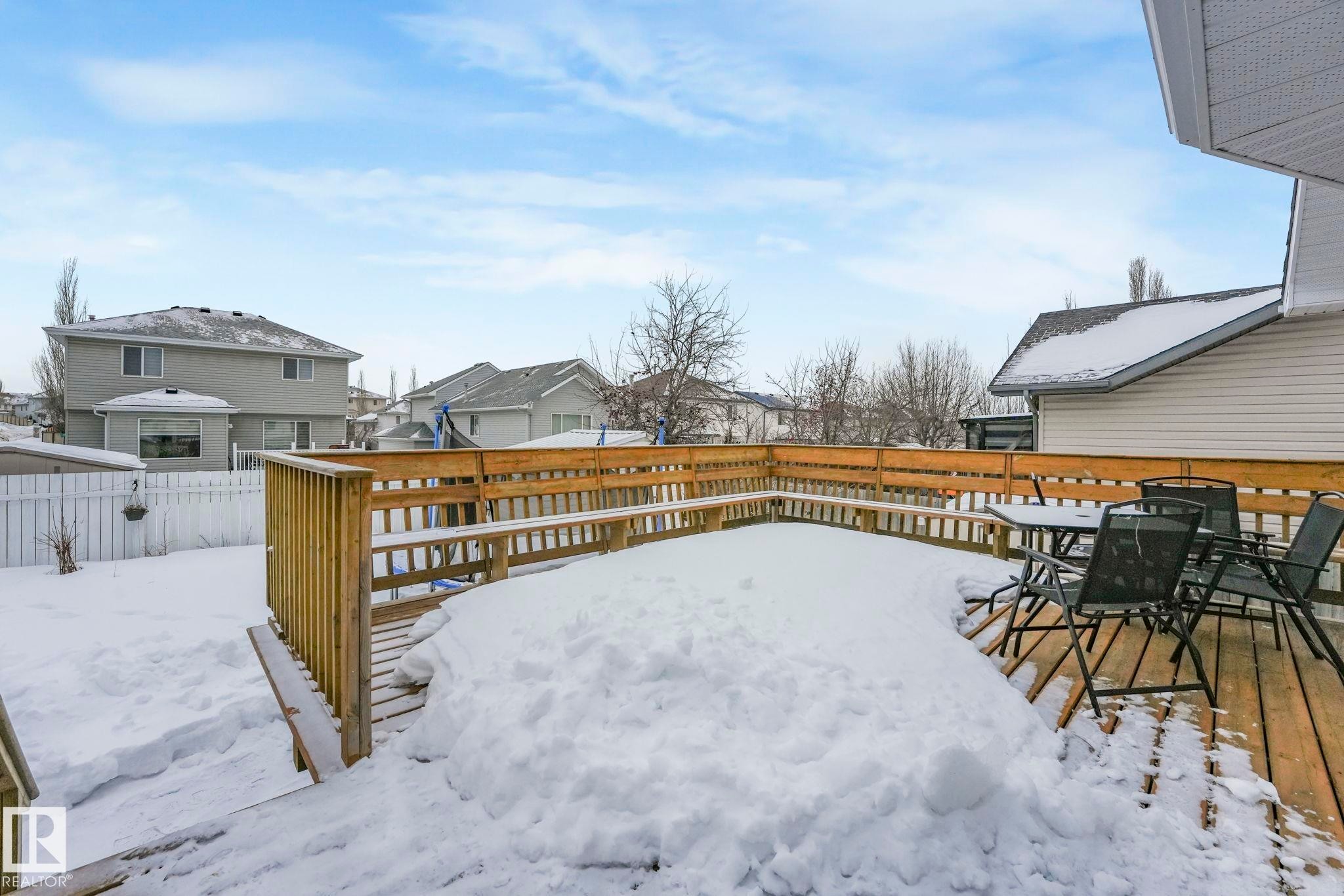 Yard covered in snow with a deck, a fenced backyard, a residential view, and outdoor dining space - 4720 150 Avenue, Edmonton, AB - Outdoor With Exterior