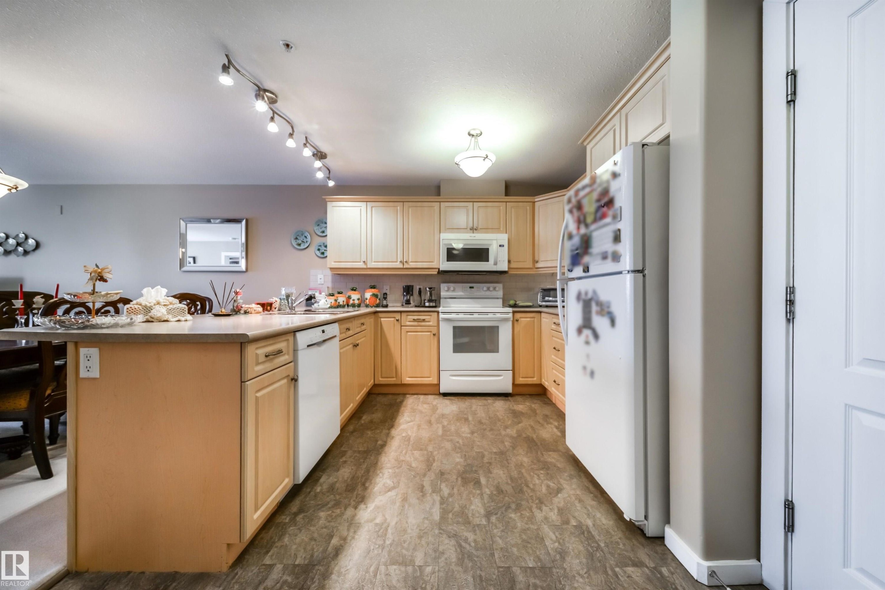 Kitchen featuring a peninsula, white appliances, light wood finish cabinetry, decorative backsplash, and a kitchen breakfast bar - 237 278 Suder Greens Drive, Edmonton, AB - Indoor Photo Showing Kitchen With Double Sink