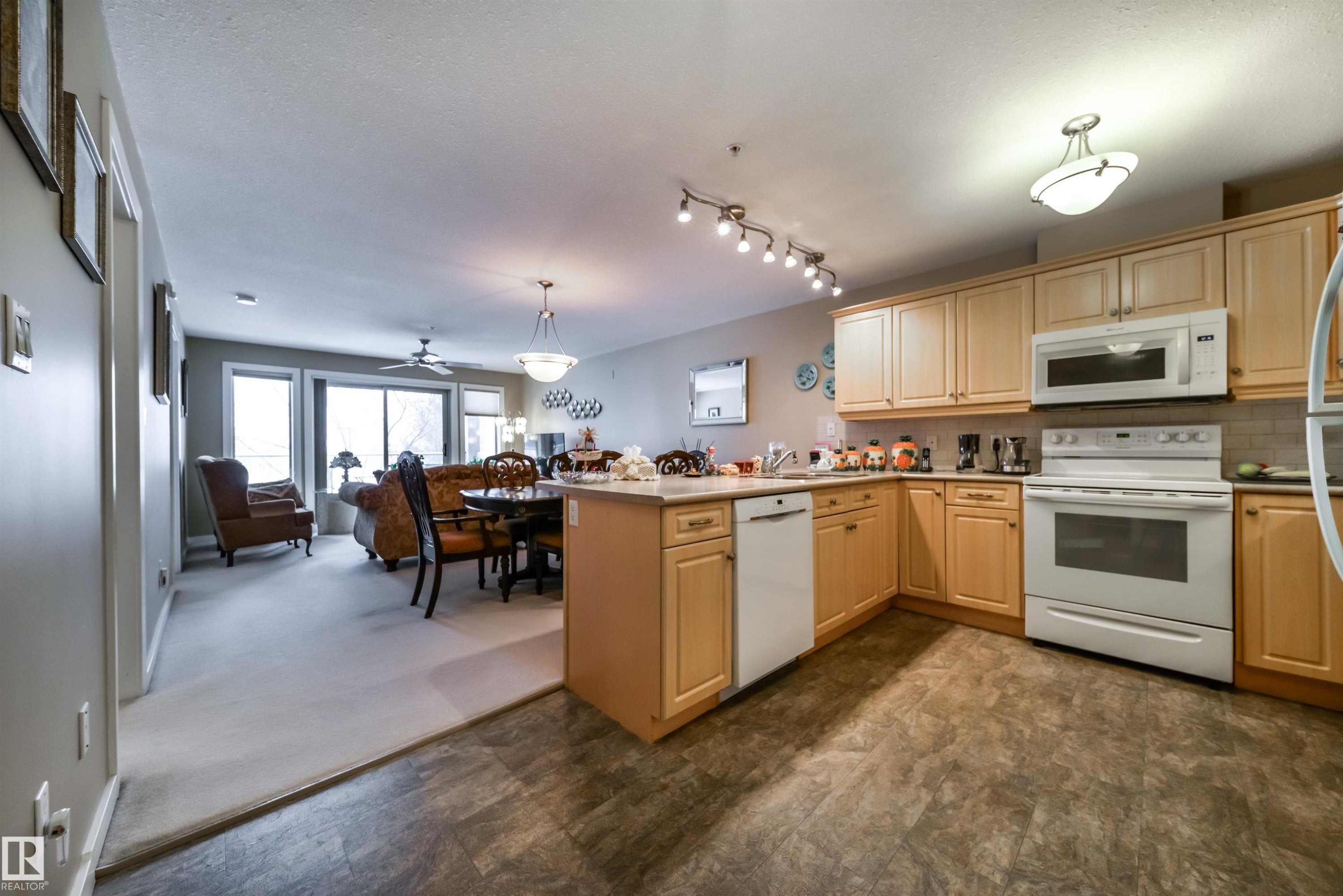 Kitchen with white appliances, a peninsula, open floor plan, decorative light fixtures, and light wood finish cabinets - 237 278 Suder Greens Drive, Edmonton, AB - Indoor Photo Showing Other Room
