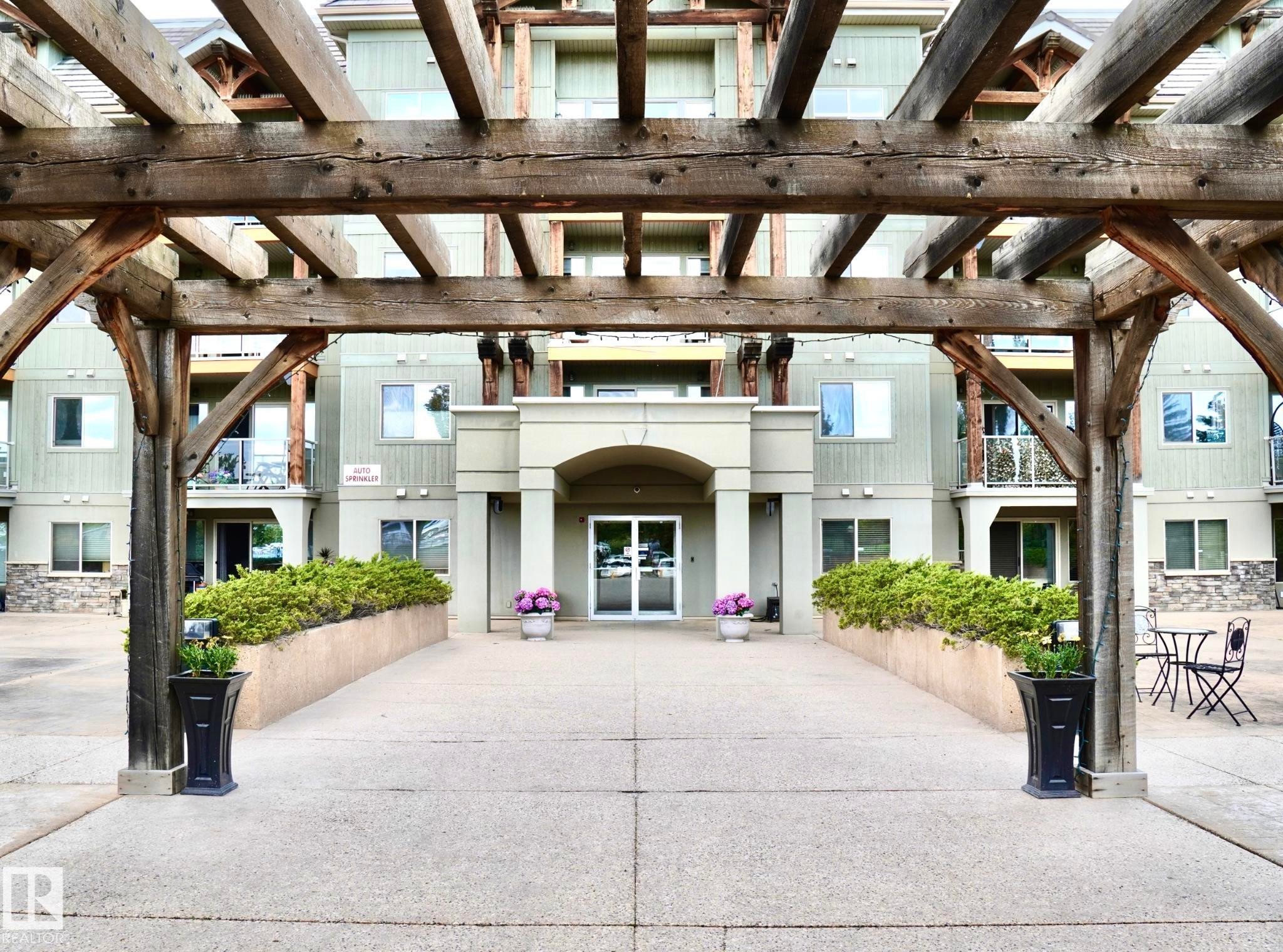Building entrance framed by a substantial wood pergola, featuring a concrete walkway leading to the main doors - 237 278 Suder Greens Drive, Edmonton, AB - Outdoor With Facade