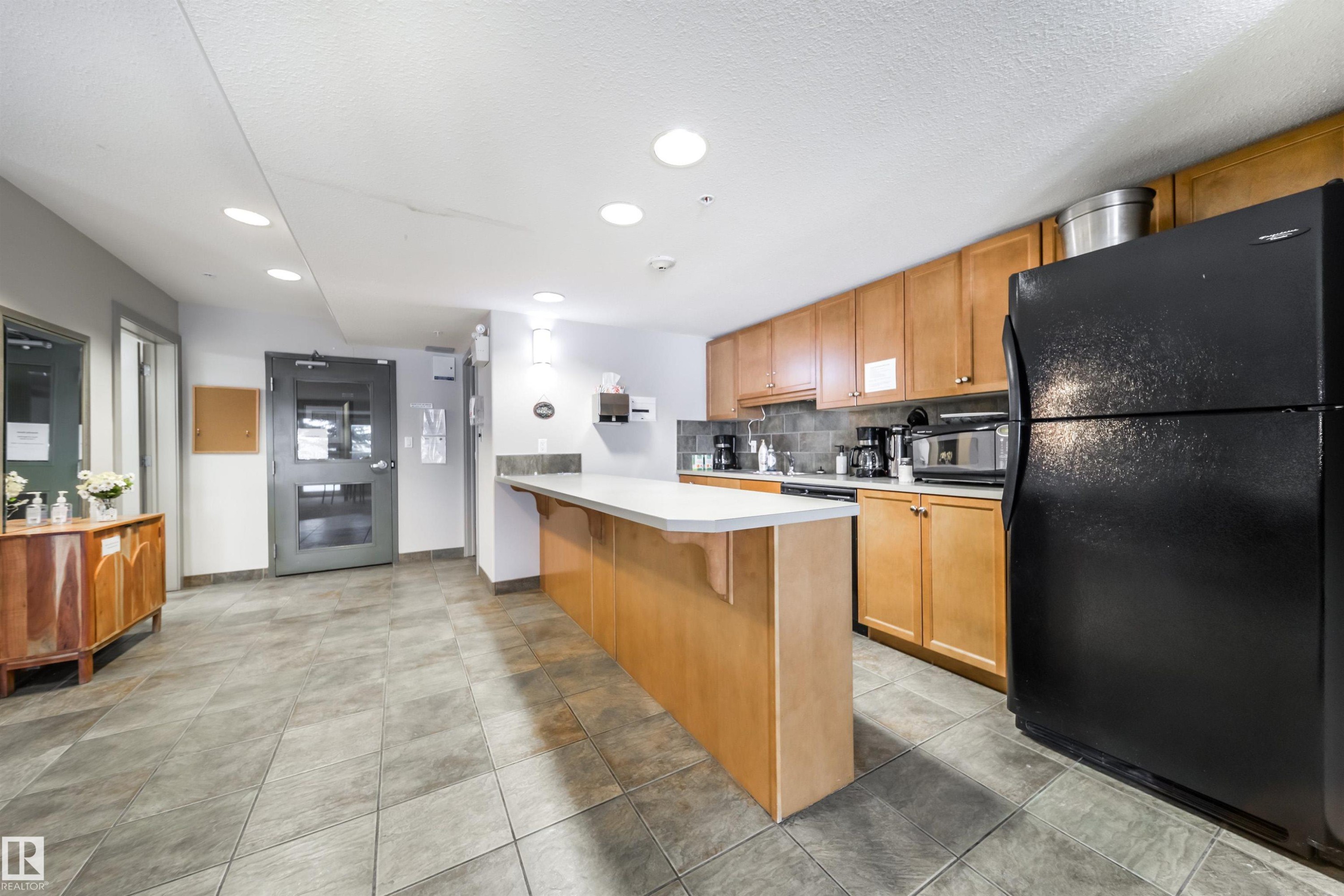 Kitchen featuring black appliances, a kitchen breakfast bar, light countertops, recessed lighting, and a peninsula - 237 278 Suder Greens Drive, Edmonton, AB - Indoor Photo Showing Gym Room