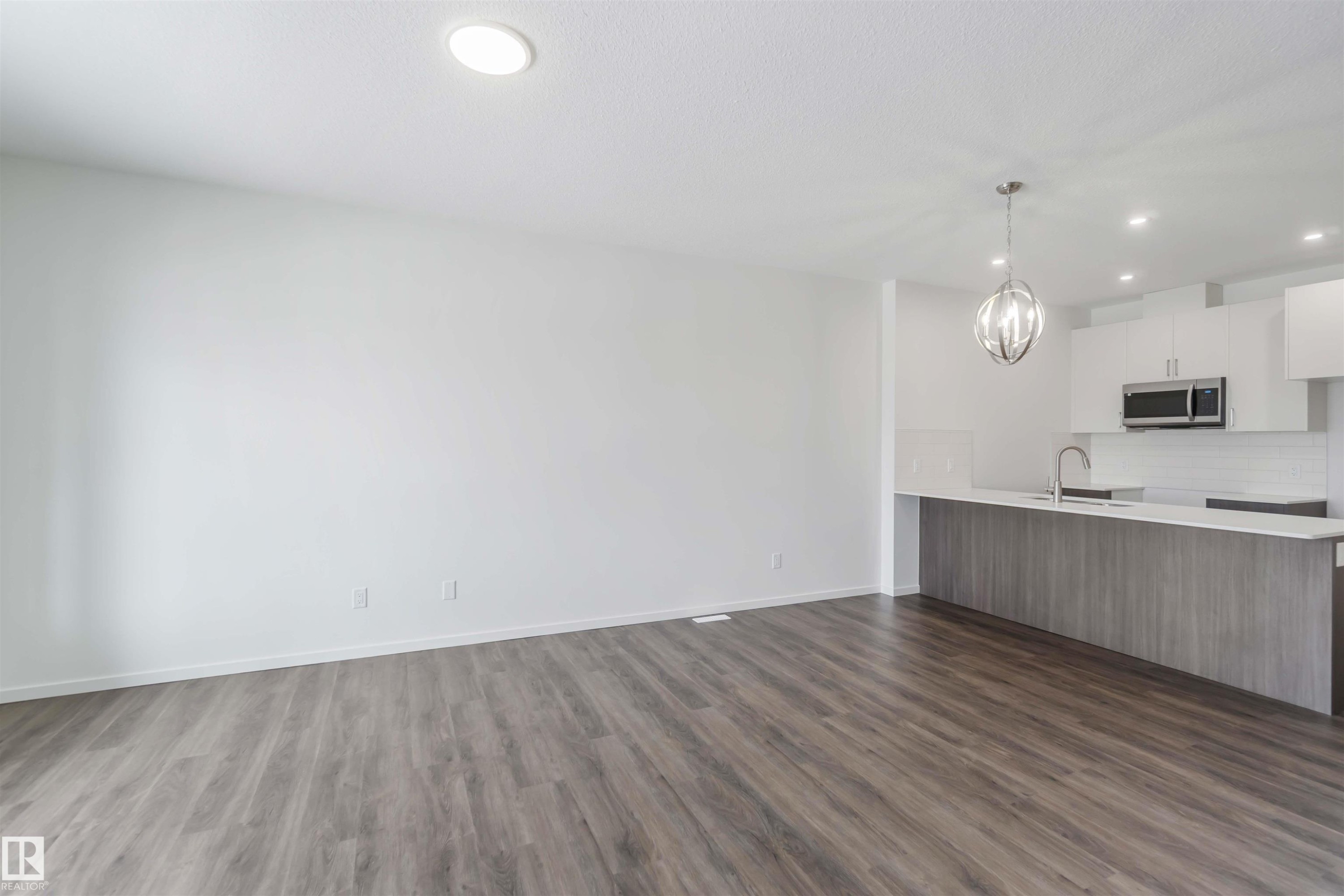 Kitchen featuring white cabinets, modern cabinets, a peninsula, open floor plan, and stainless steel microwave - 2467 Alces Link Link, Edmonton, AB - Indoor Photo Showing Kitchen