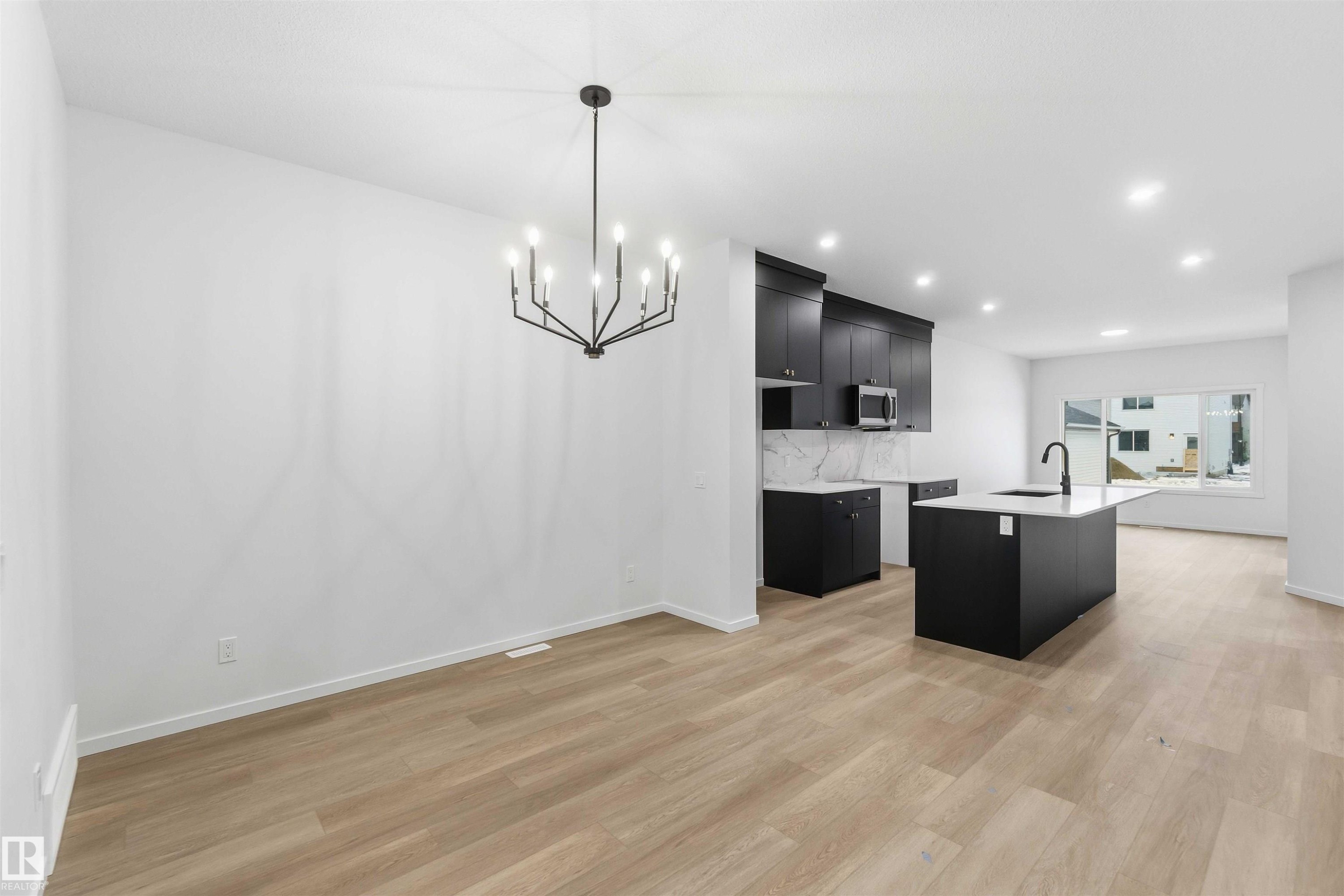 Kitchen with dark cabinets, a kitchen island with sink, light wood-style floors, suspended lighting, and light stone countertops - 8652 Edgemont Link, Edmonton, AB - Indoor Photo Showing Kitchen With Upgraded Kitchen