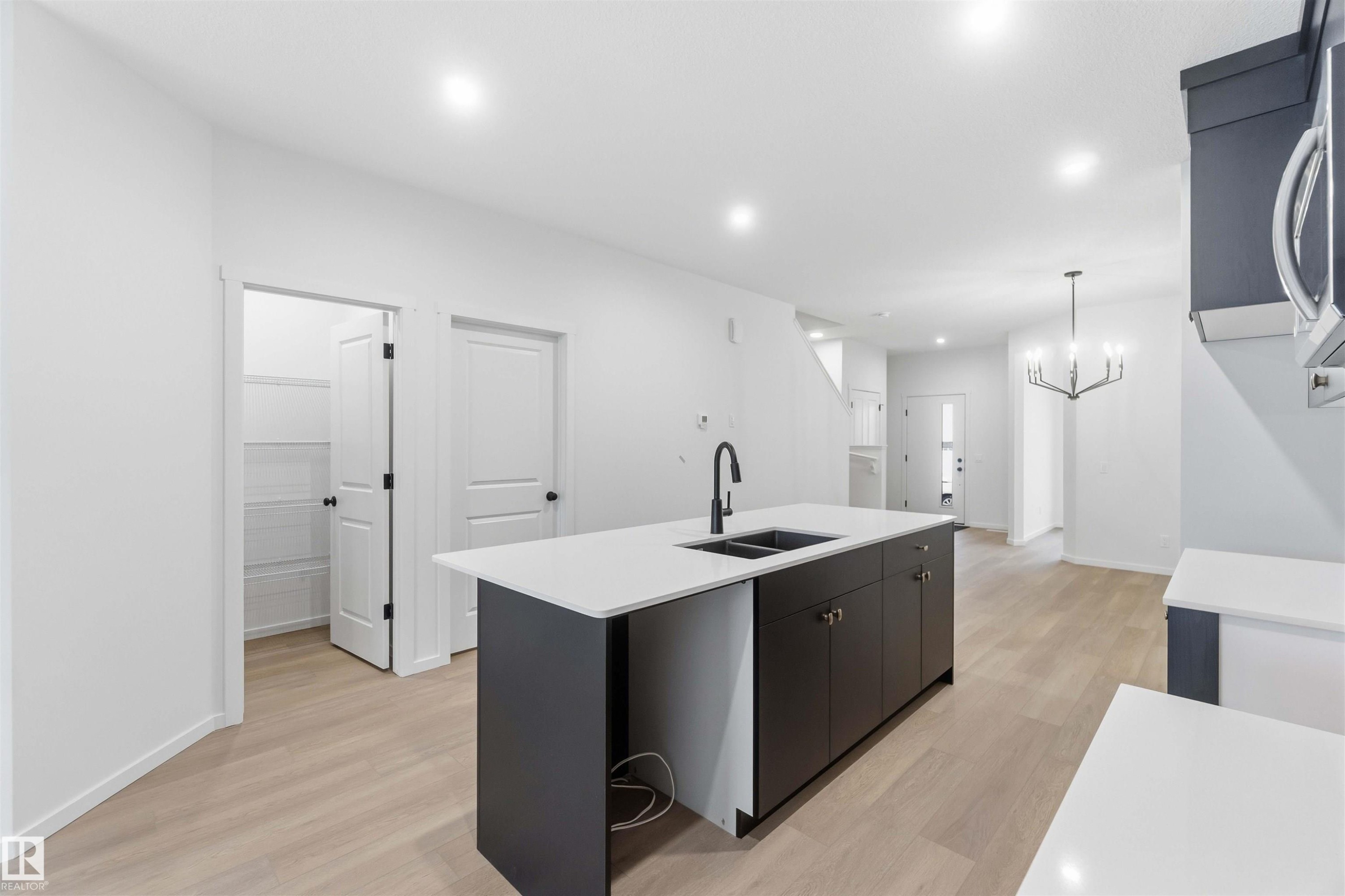 Kitchen with a kitchen island with sink, light wood finished floors, stainless steel microwave, a chandelier, and light stone countertops - 8652 Edgemont Link, Edmonton, AB - Indoor Photo Showing Kitchen With Double Sink