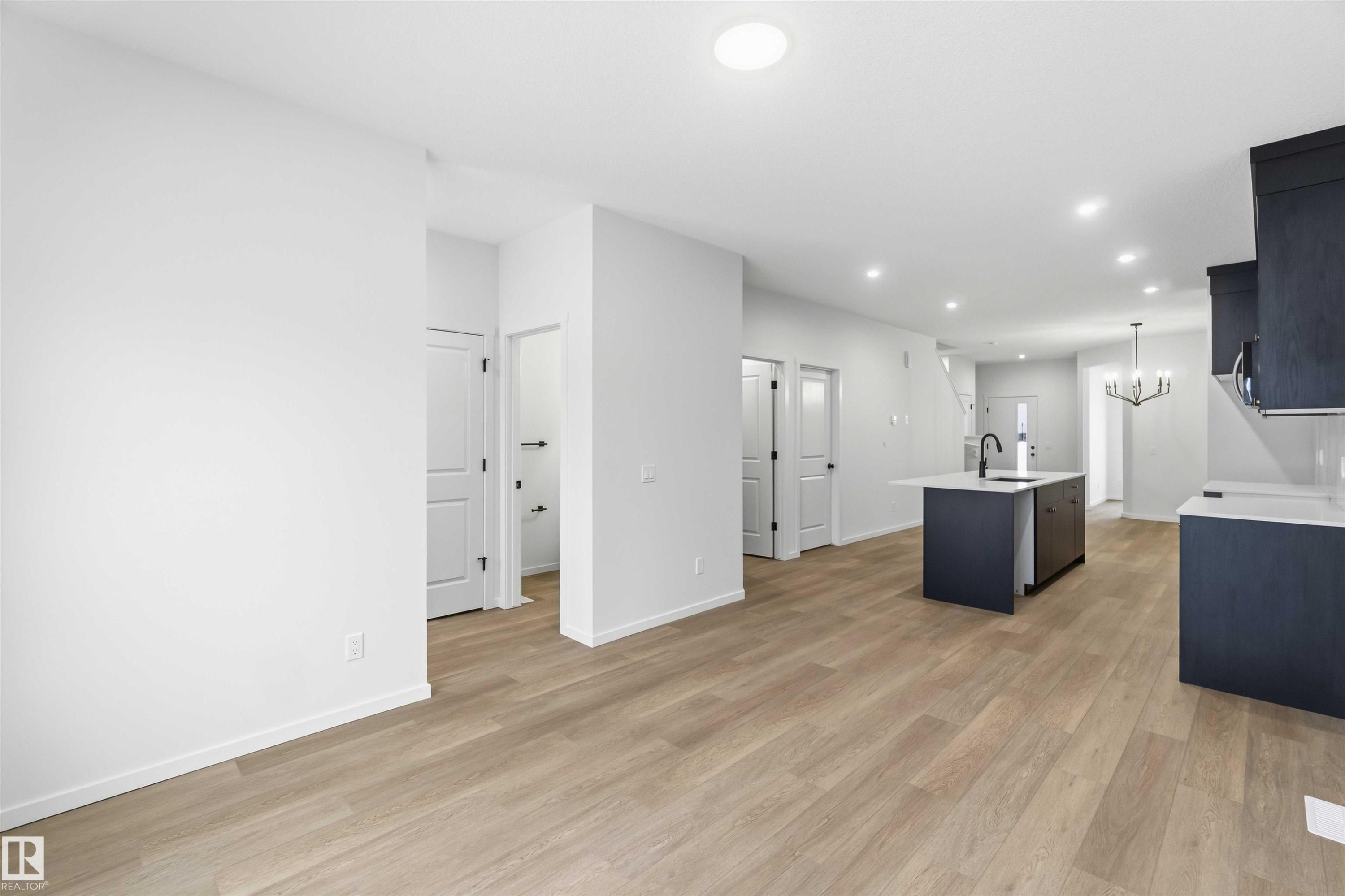 Kitchen with a chandelier, a center island with sink, light wood-style floors, and light stone countertops - 8652 Edgemont Link, Edmonton, AB - Indoor