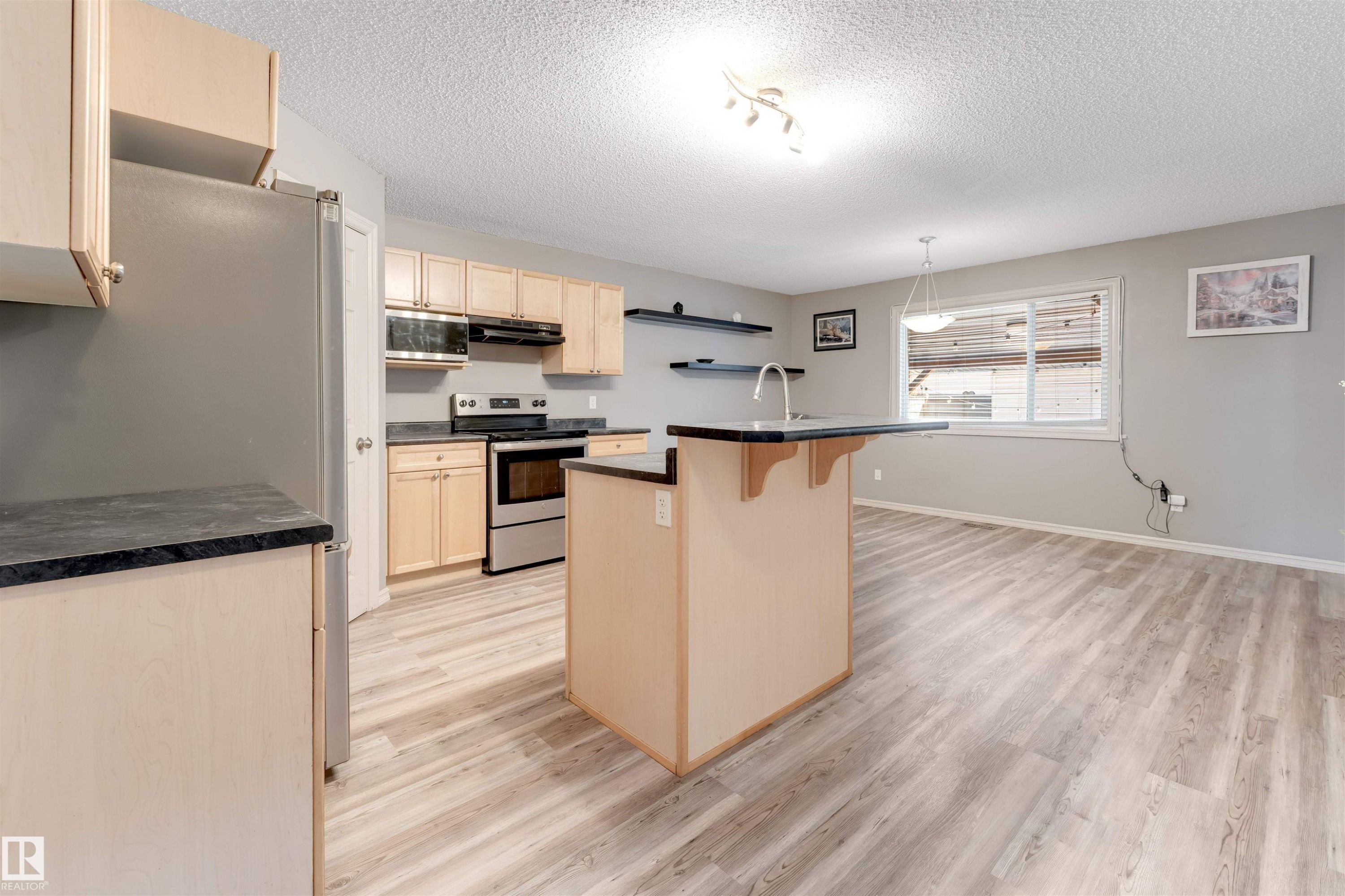 Kitchen with light wood finish cabinetry, a center island with sink, a breakfast bar, stainless steel appliances, and light wood-style flooring - 1157 37 Avenue, Edmonton, AB - Indoor Photo Showing Kitchen