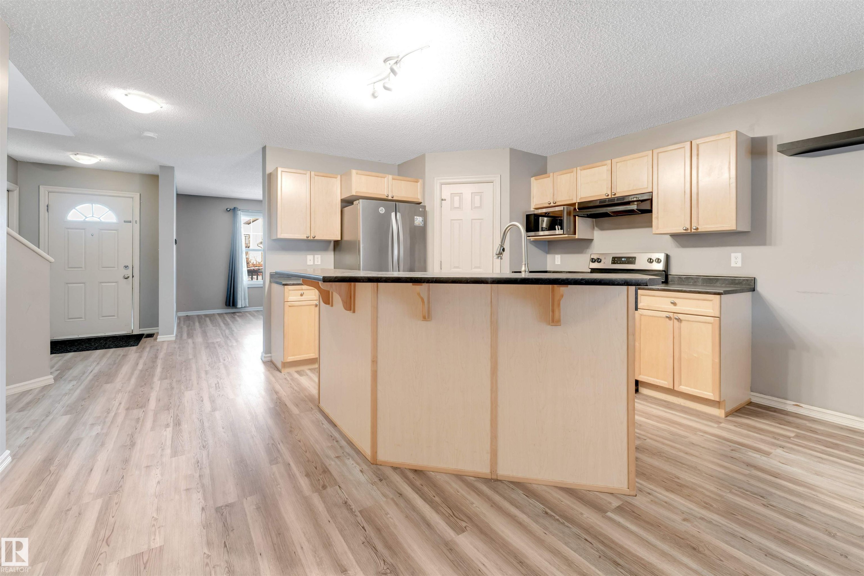 Kitchen with a kitchen bar, light wood finish cabinetry, a center island with sink, stainless steel appliances, and a textured ceiling - 1157 37 Avenue, Edmonton, AB - Indoor Photo Showing Kitchen